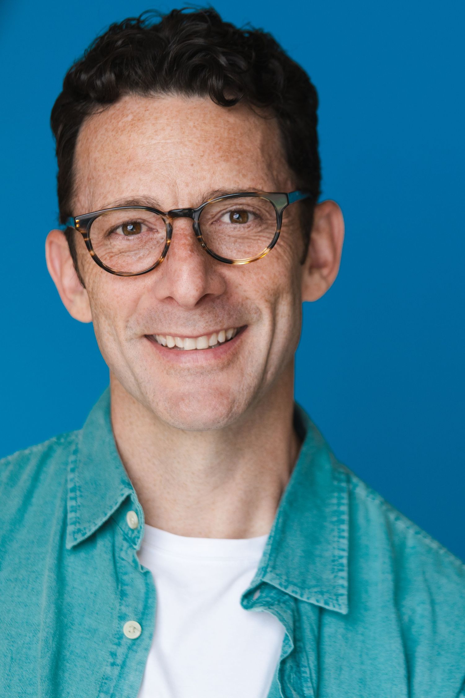 Series of casual portrait shots with glasses and denim shirt against bright blue background.
