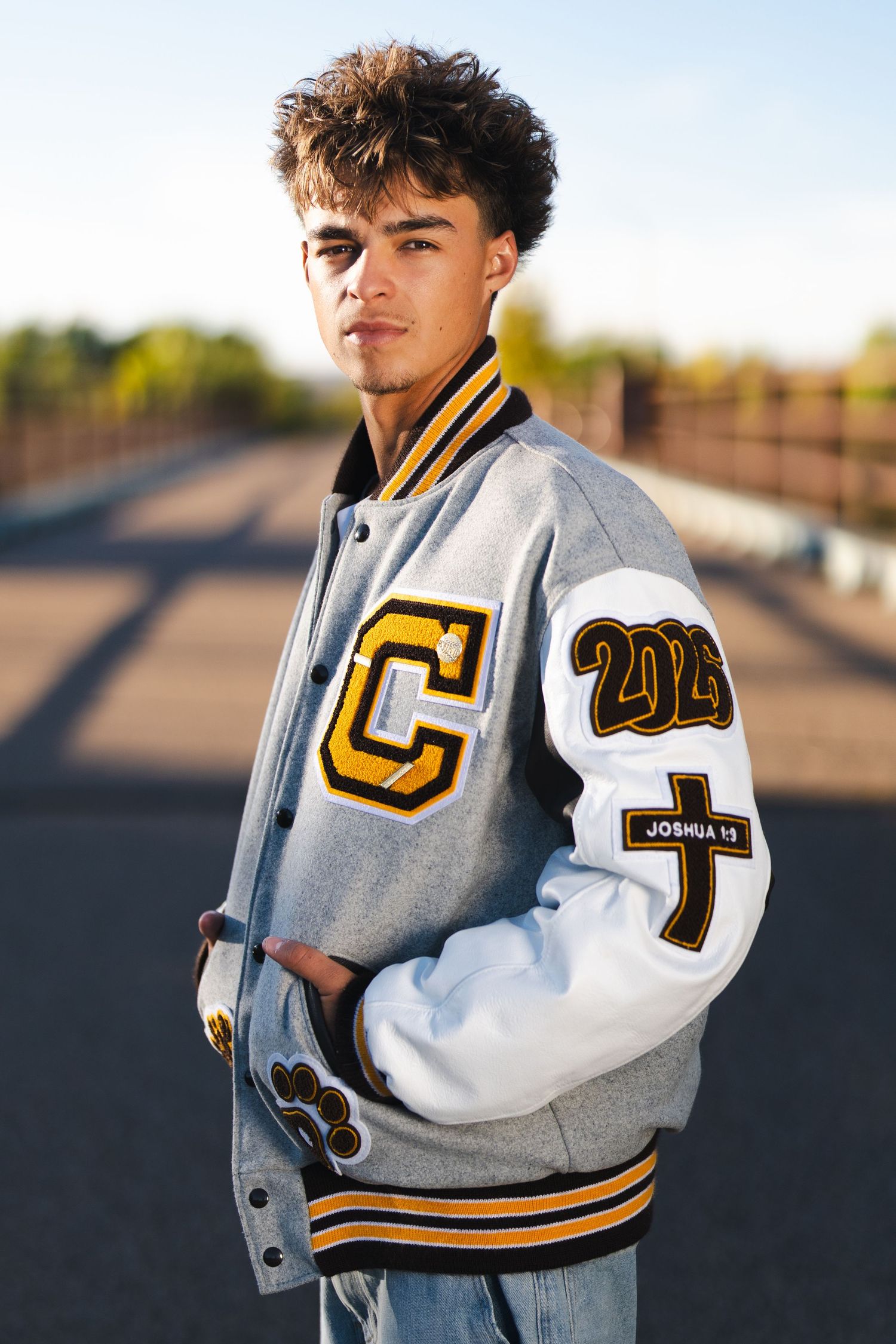 Grey and white varsity letterman jacket with yellow numbers and patches.