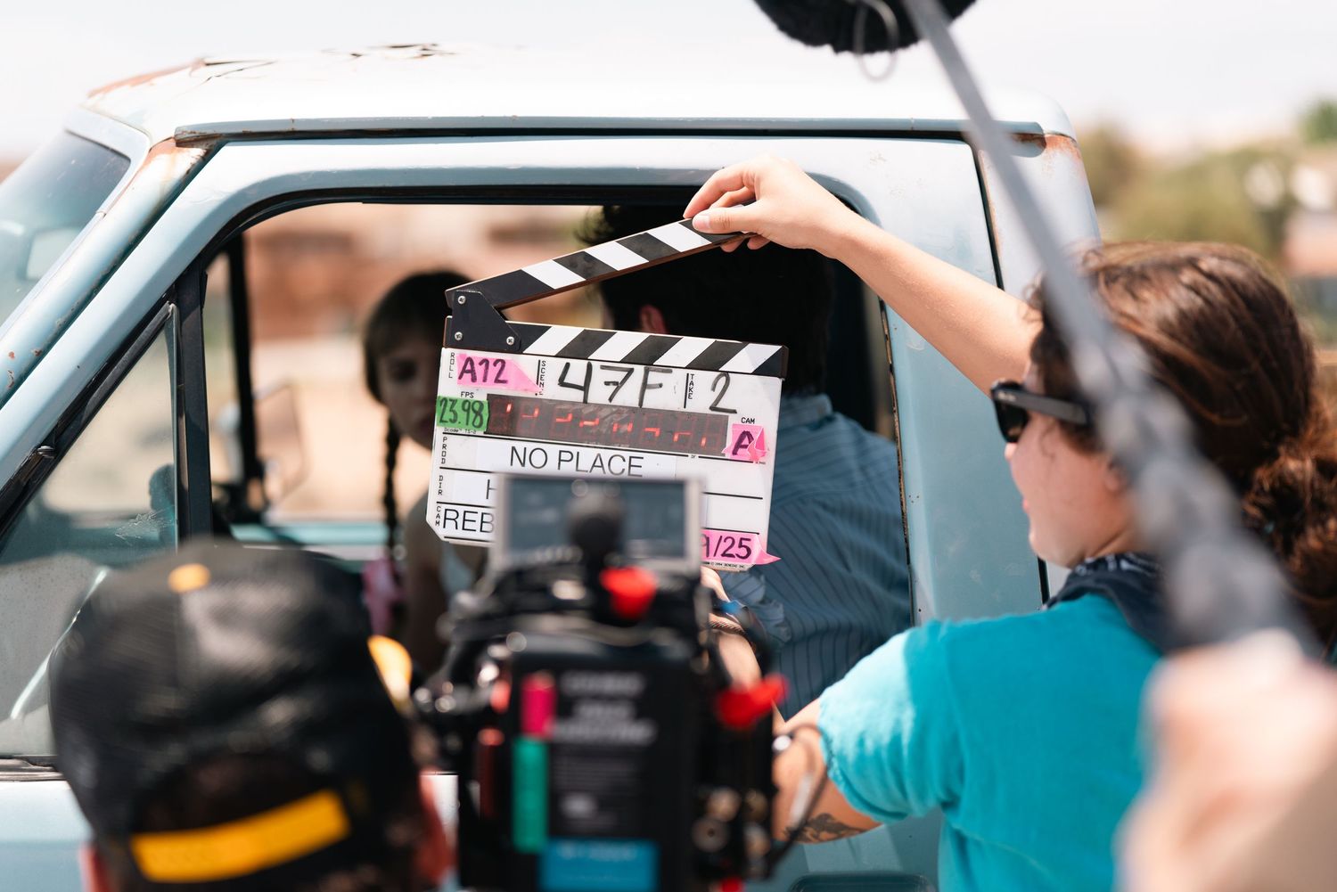 Film crew shooting scene through car window with clapperboard.