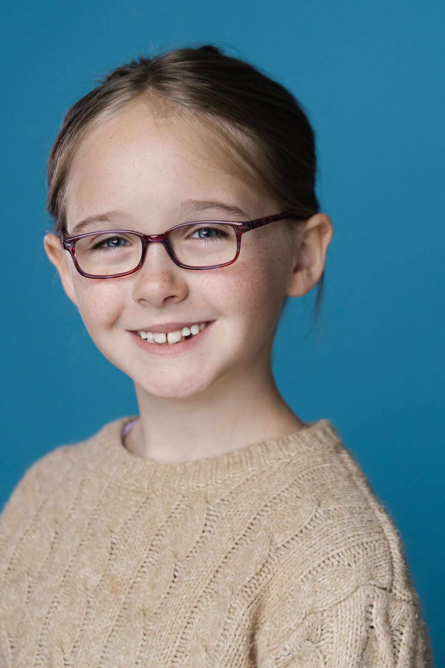 Warm portrait series in beige sweater against blue background showing genuine smiles.