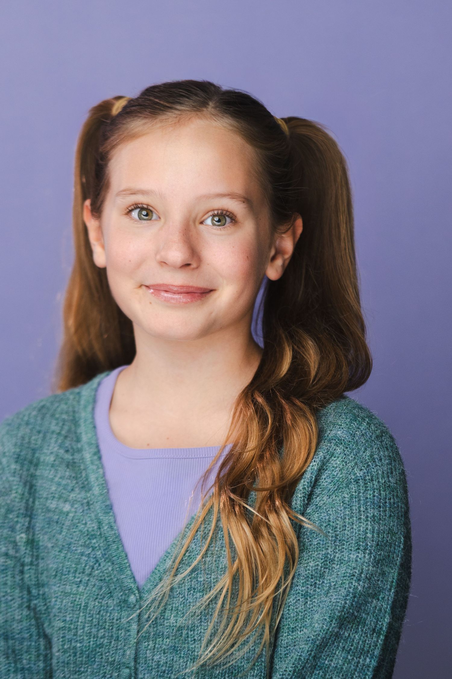 Portrait of youth with pigtails wearing teal sweater against purple background.