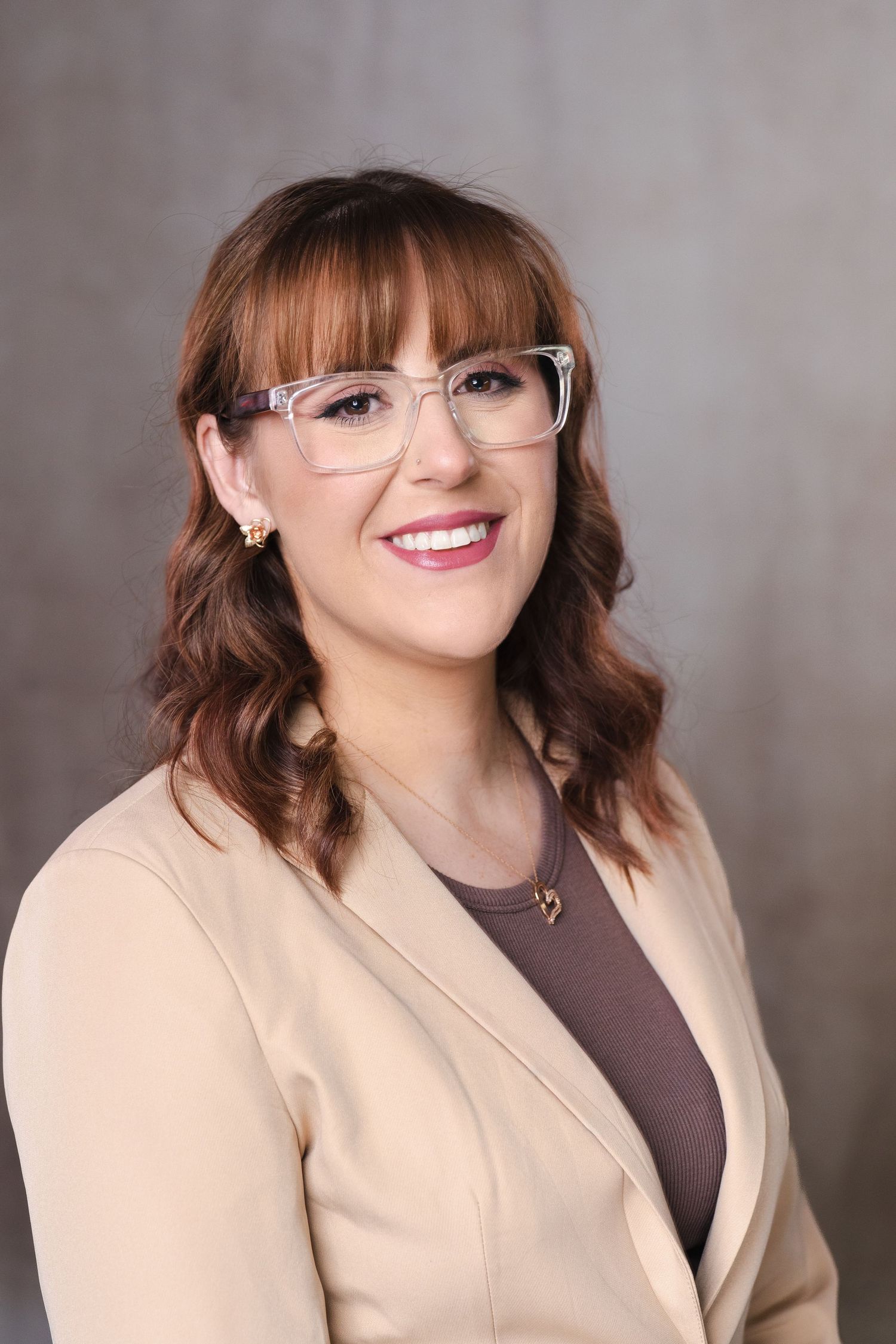 Professional portrait of person wearing glasses and beige blazer with warm smile.