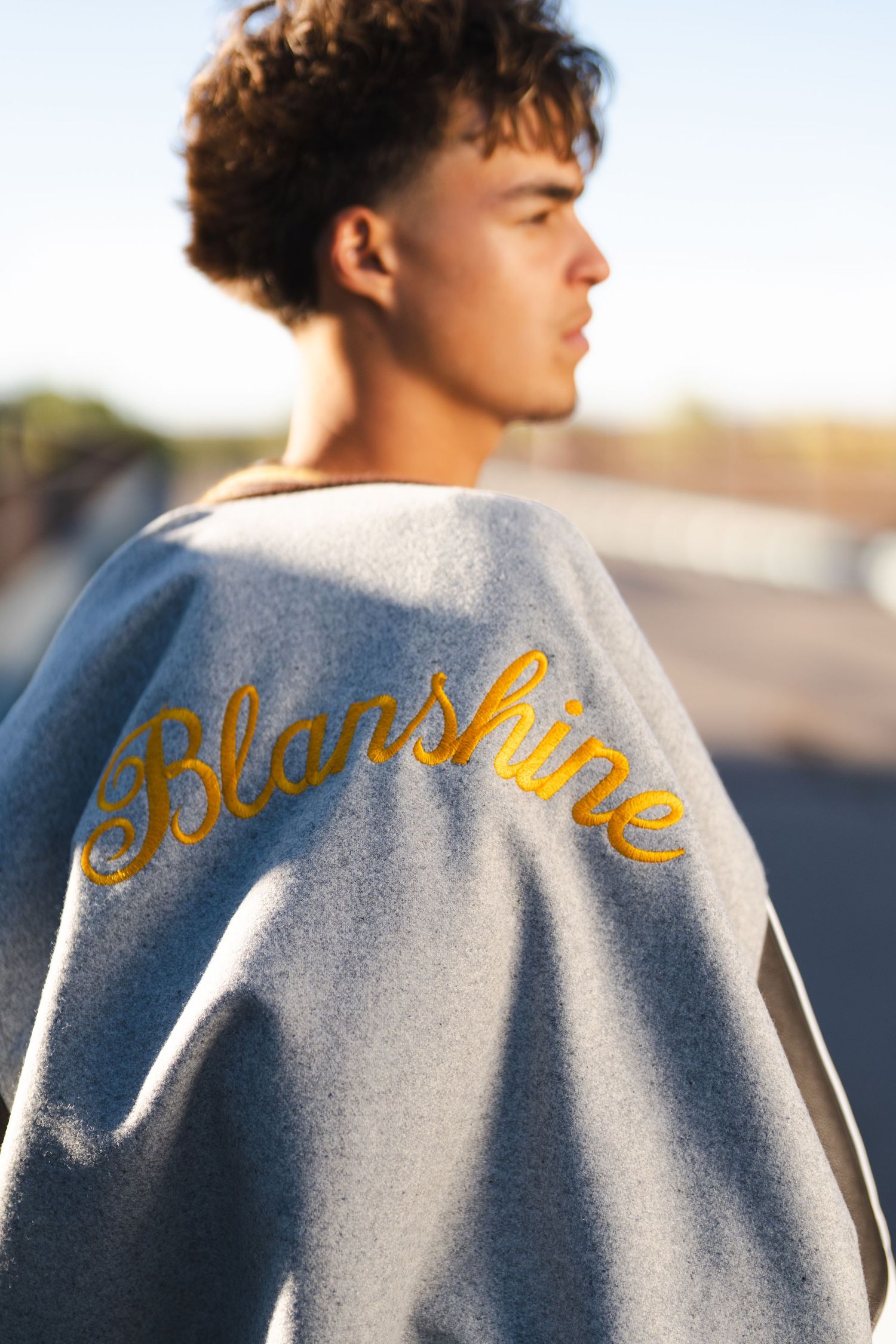 Grey varsity jacket with gold lettering embroidered across the back.