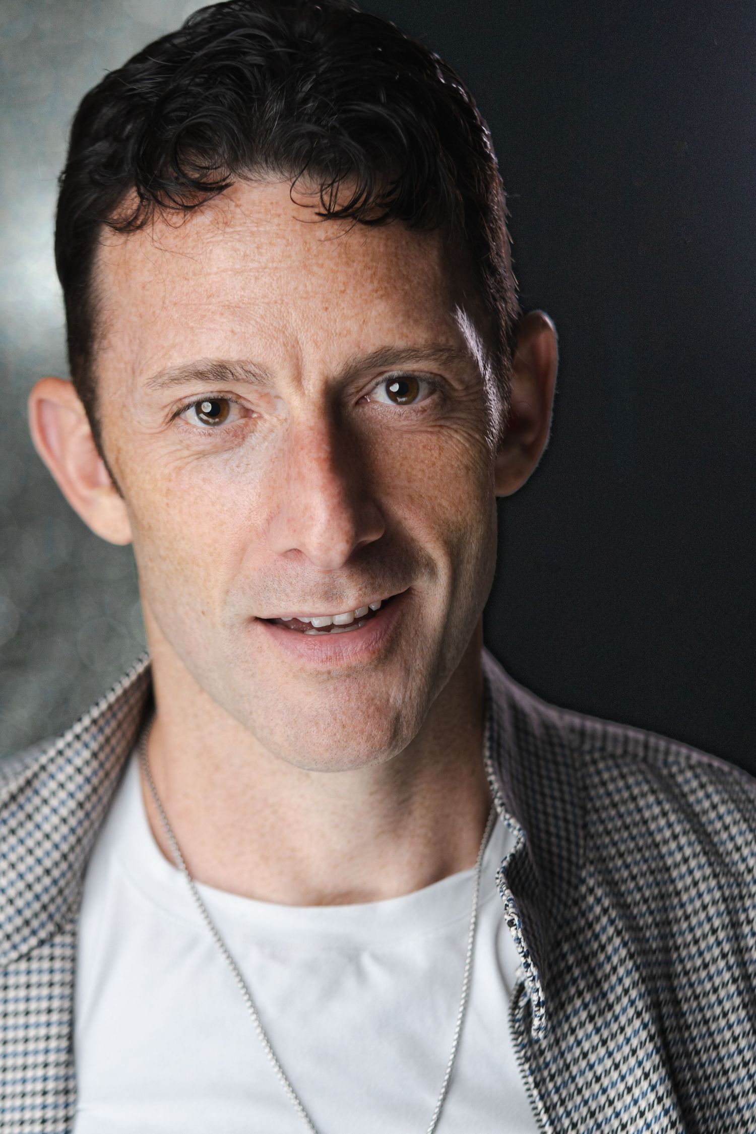 Professional headshots showing different expressions while wearing checkered jacket and white shirt.