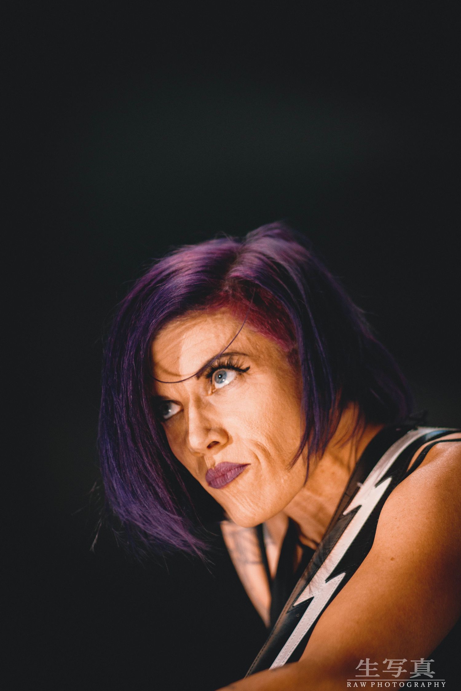 Close-up profile shot of performer with purple hair in dramatic lighting.