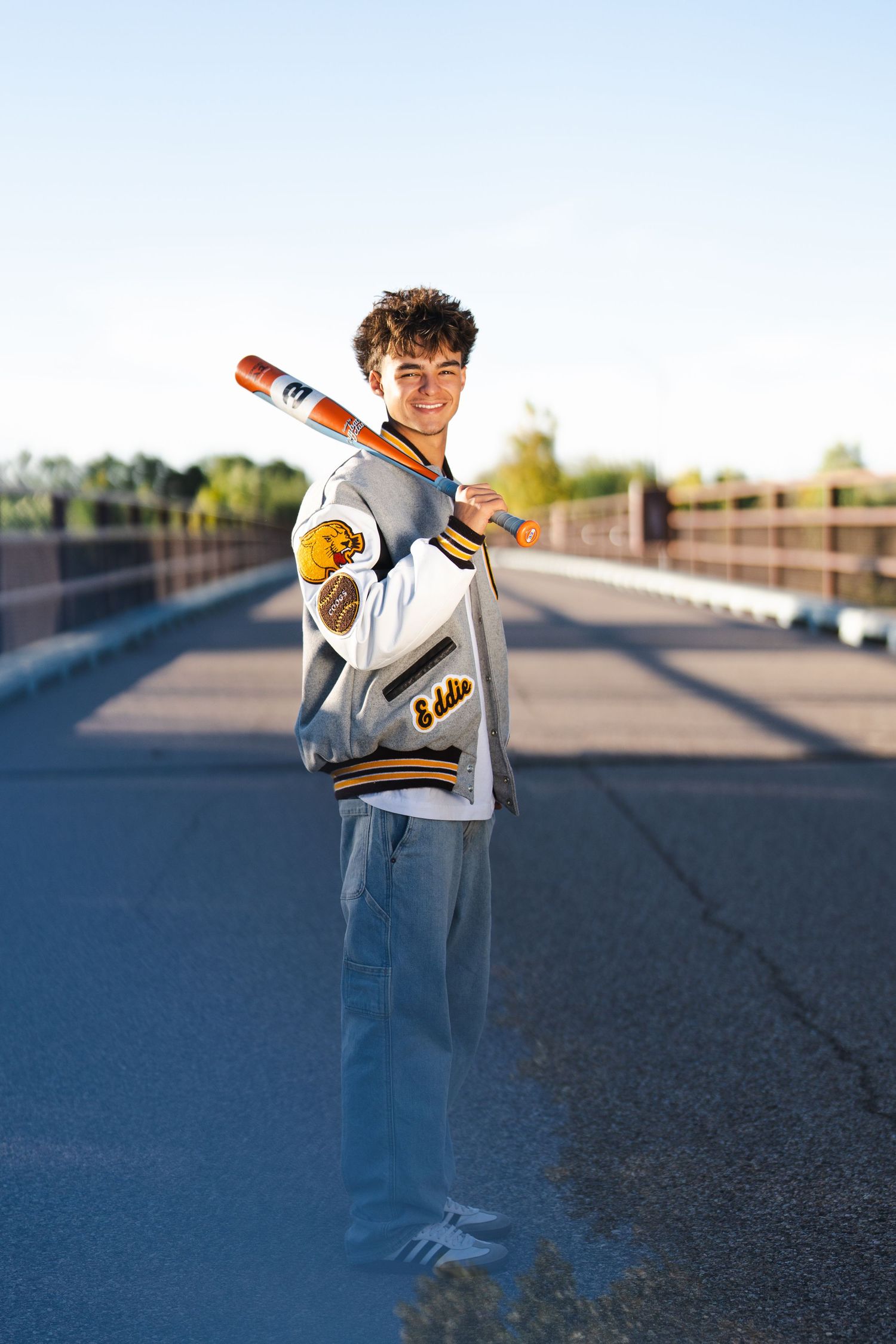 New Mexico Photographer - Graduation Person in varsity jacket poses with baseball bat on empty road at sunset.