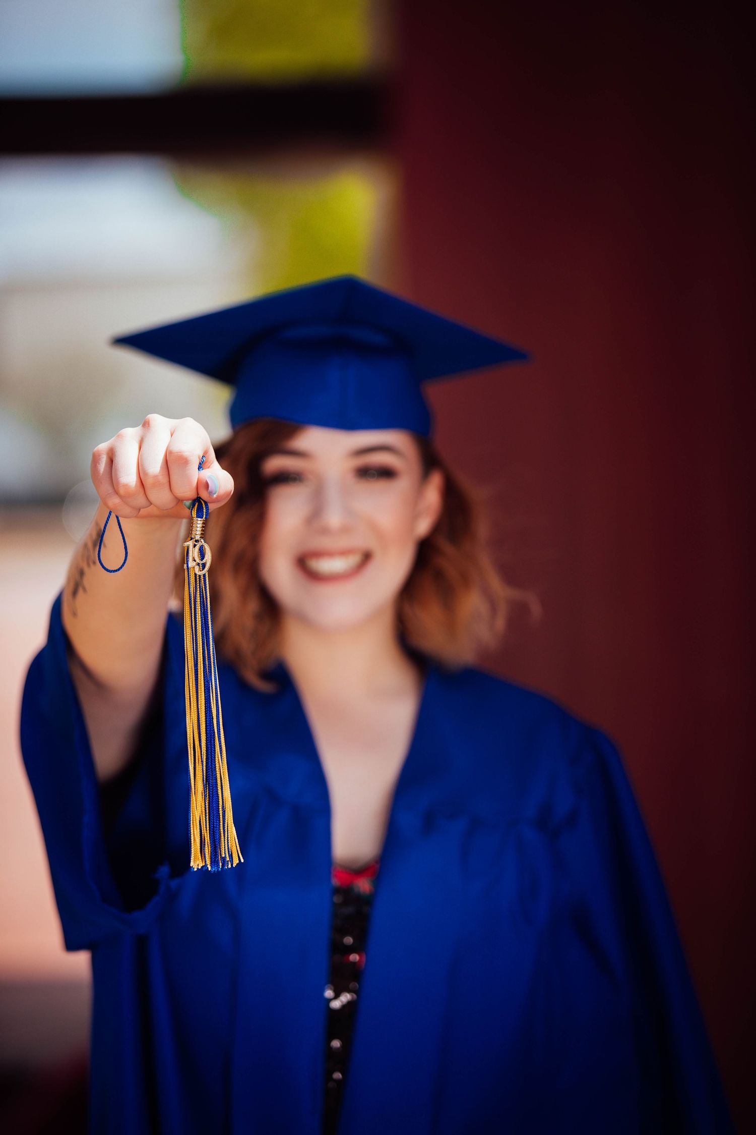 New Mexico Photographer - GraduationGraduate in blue cap and gown holds up graduation tassel with gold accents during commencement ceremony.