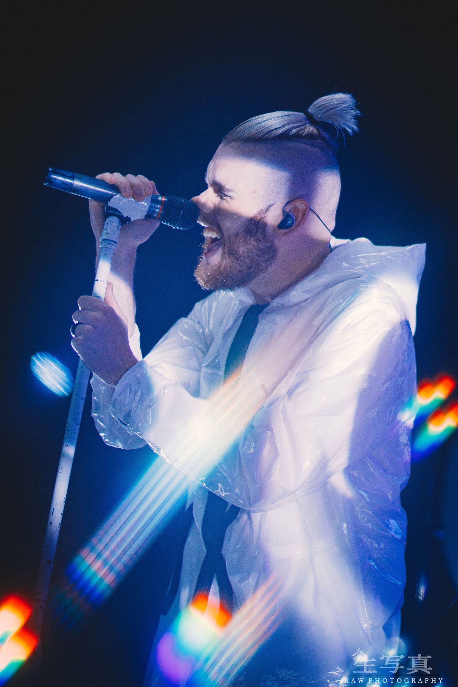 Concert performer in white outfit singing passionately on stage with dramatic blue lighting and lens flares.