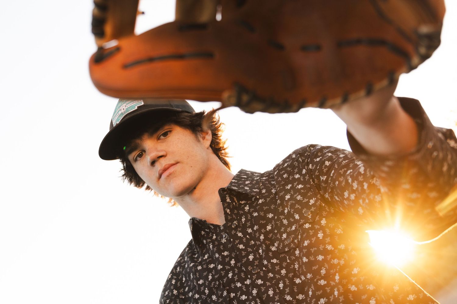 Silhouette figure poses with baseball glove against bright sunburst background.