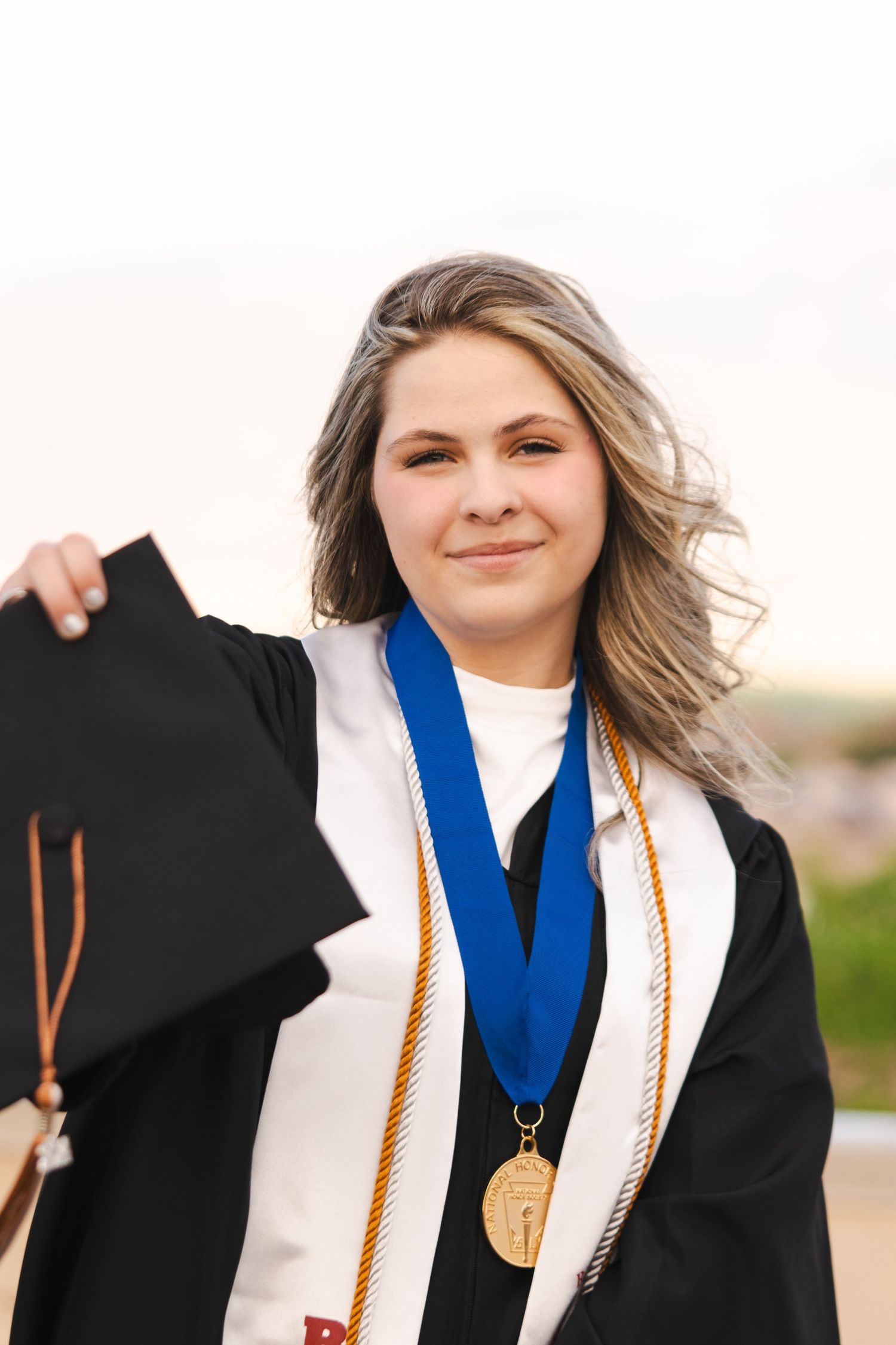 New Mexico Photographer - Graduate wearing black cap and gown with blue honor cord and gold medal smiling outdoors.