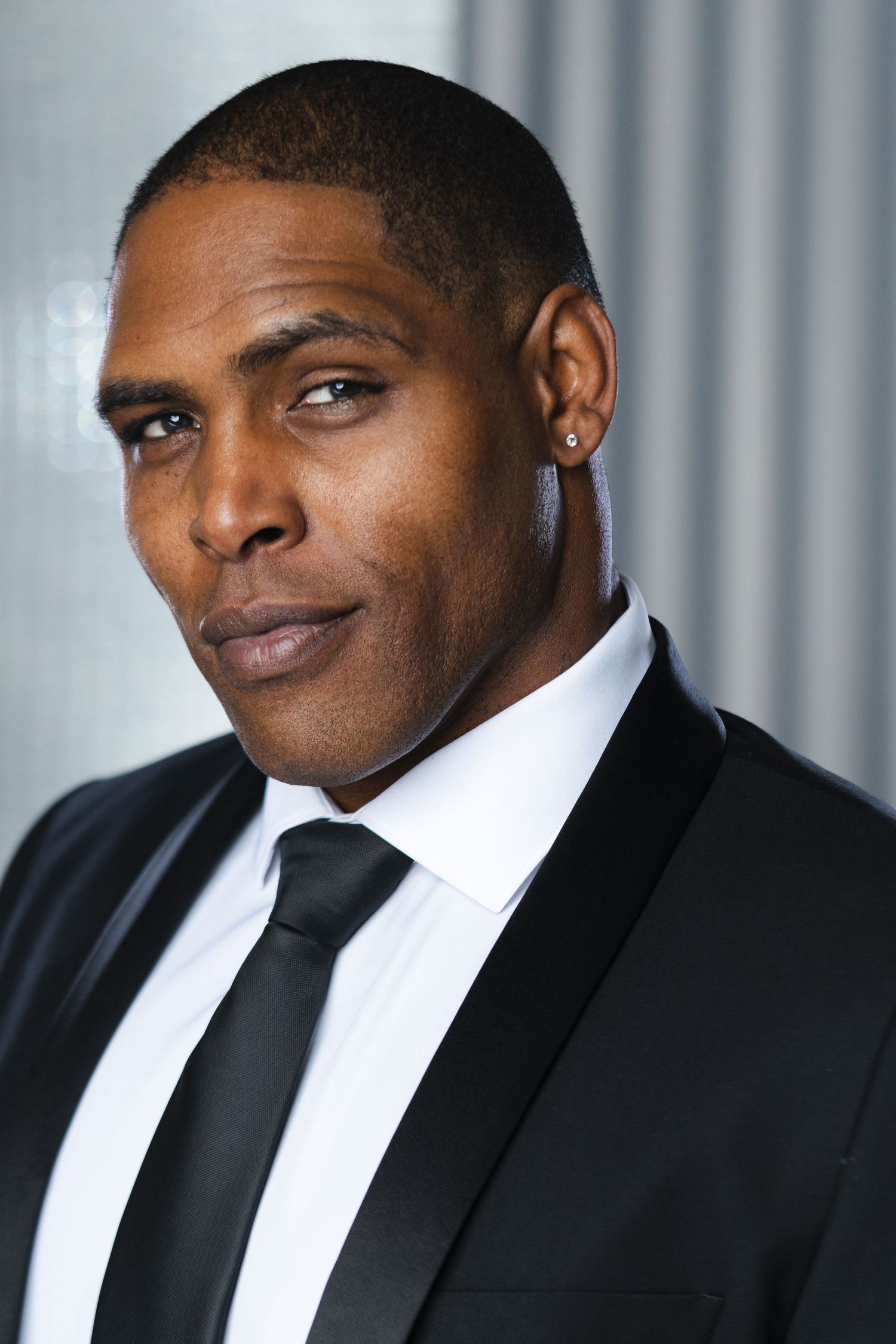 Professional portrait of person in black suit and tie against grey background.