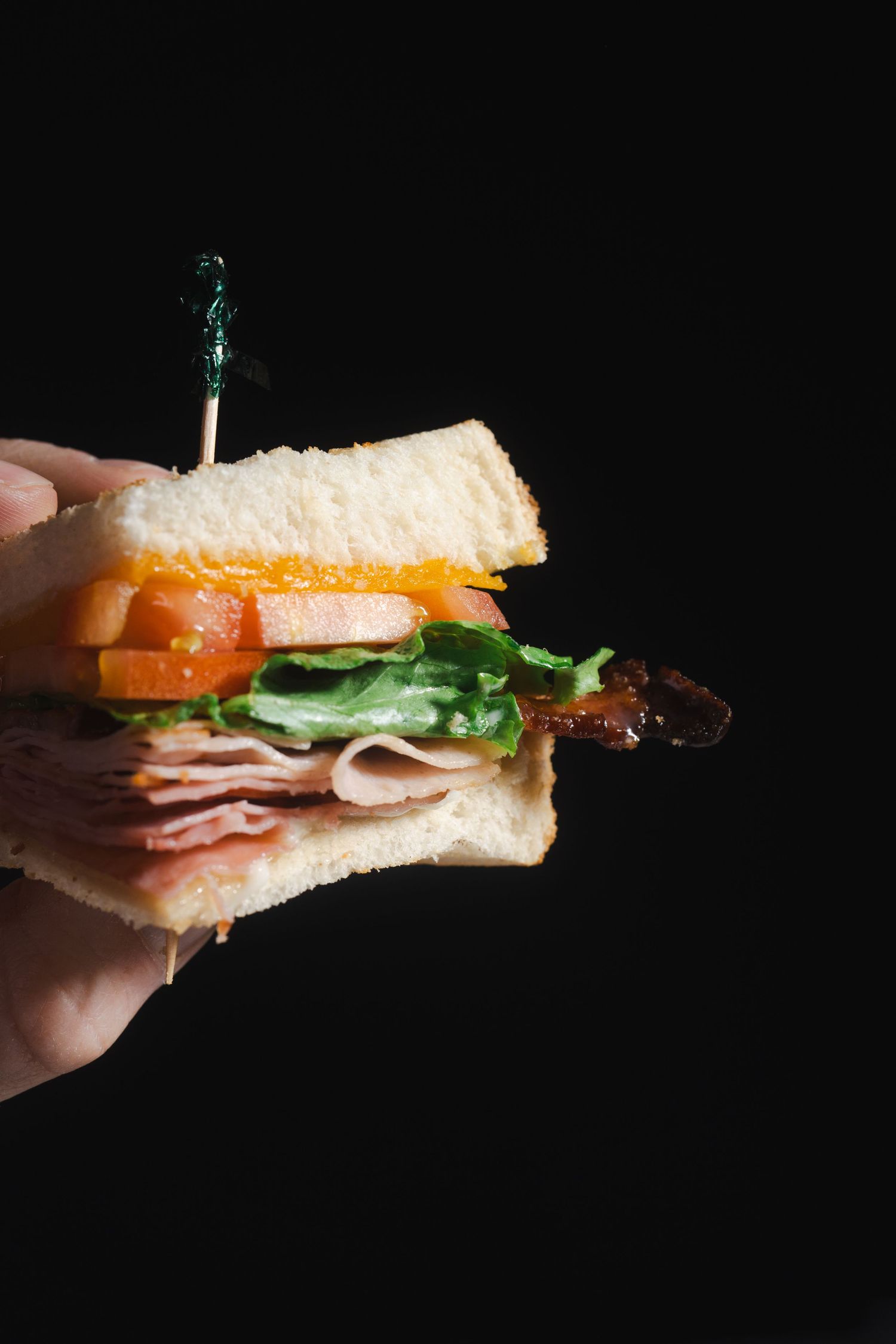 Close-up of a sandwich with sliced meat, tomatoes, and lettuce on white bread.