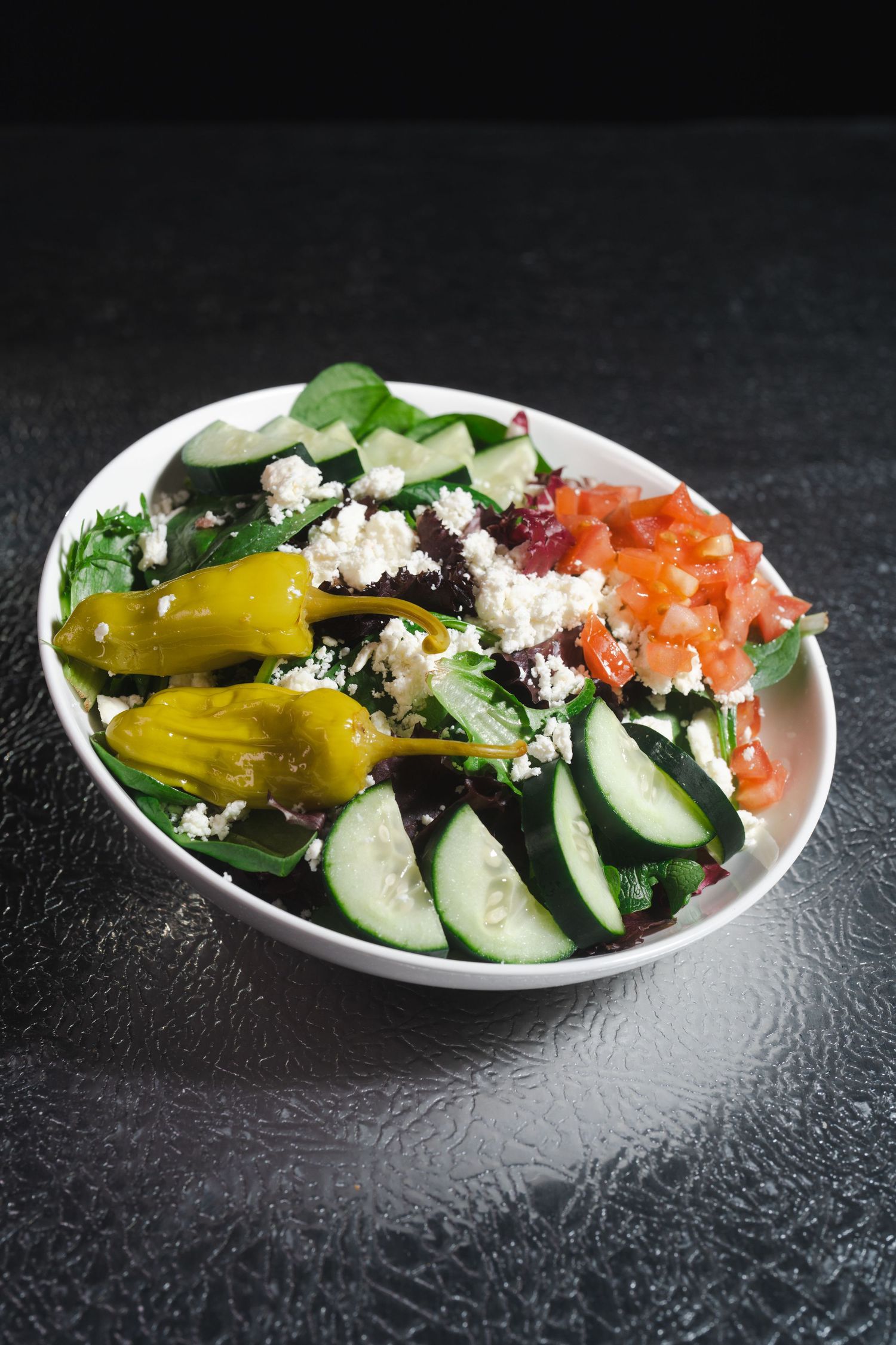Fresh Greek salad with cucumbers, feta cheese, tomatoes and pepperoncini peppers on a white plate.