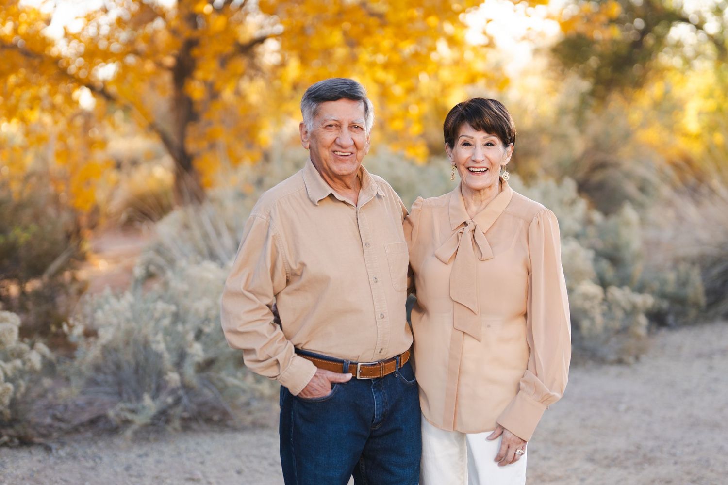 Couple poses together outdoors with golden autumn foliage in background.