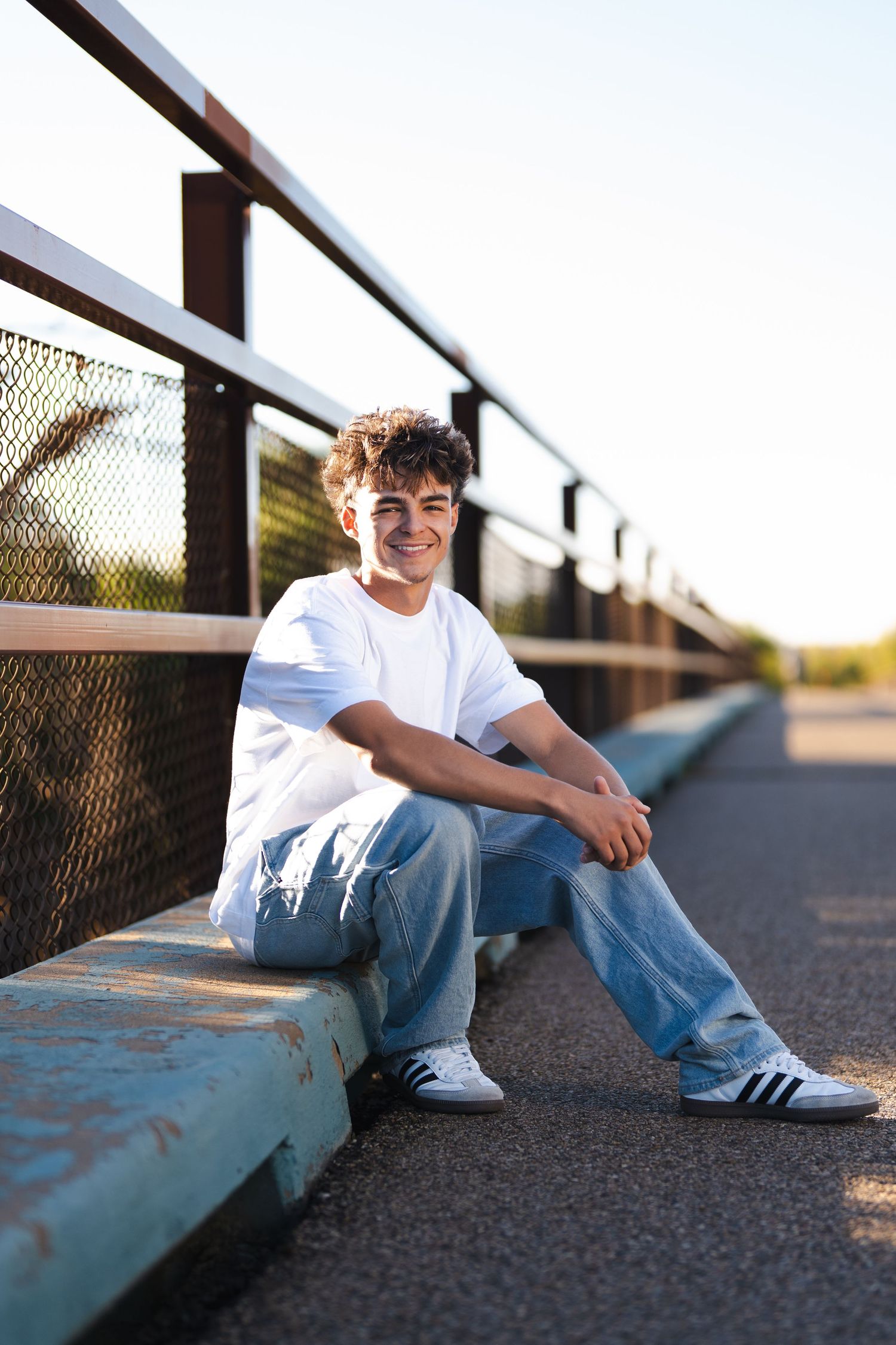 Casual portrait of someone sitting on ground wearing white t-shirt and jeans.