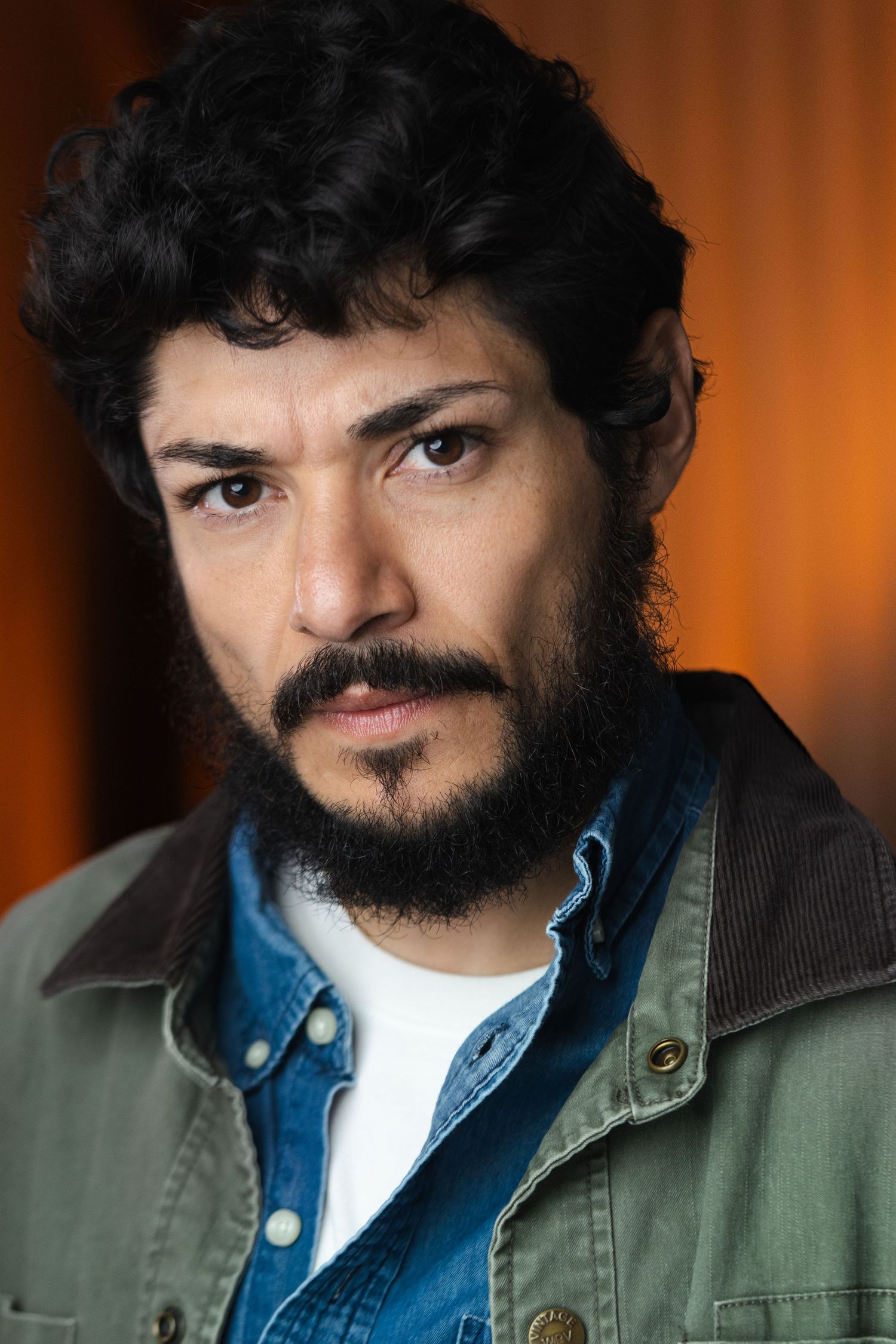 Portrait of person with dark beard wearing layered denim and olive jacket.