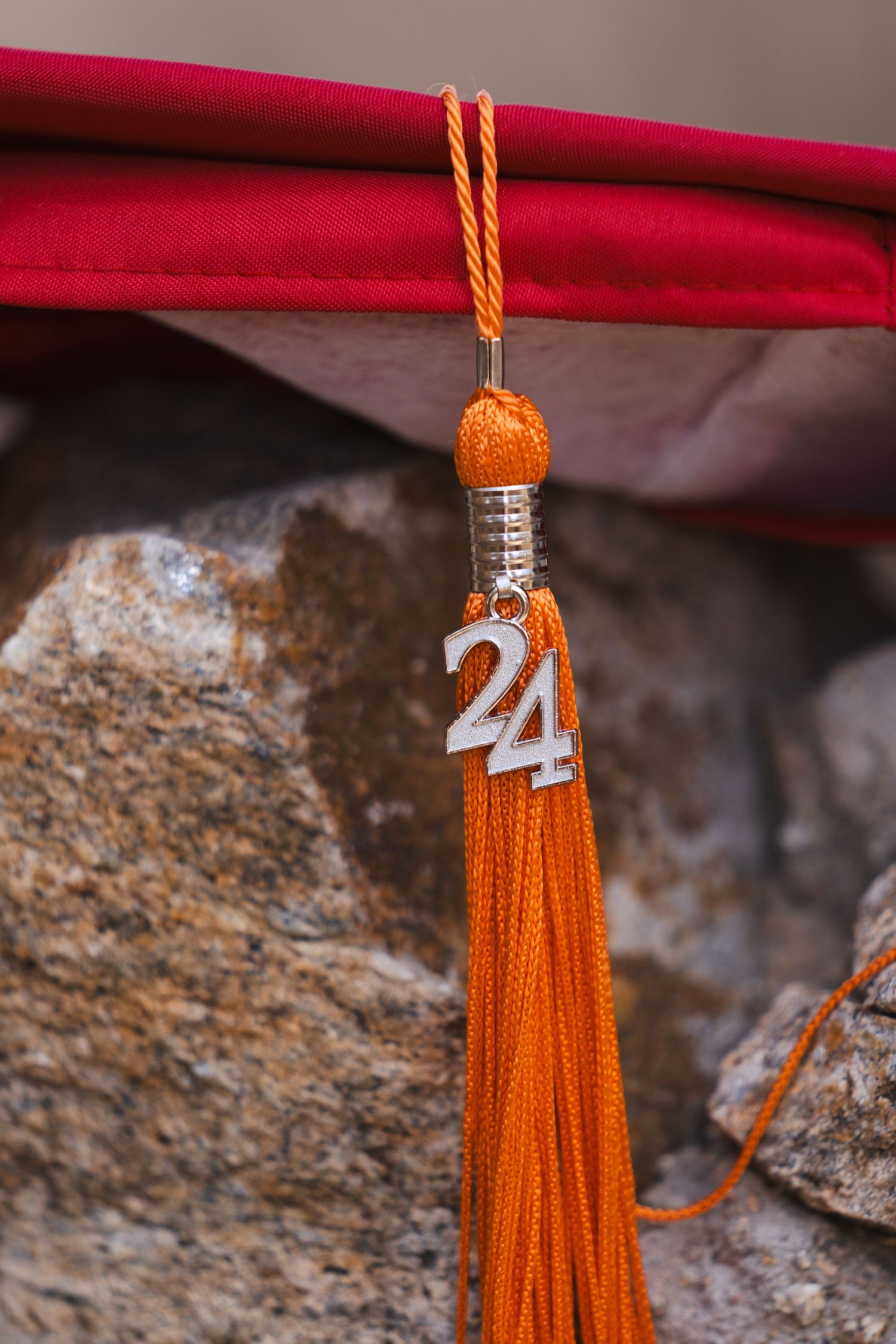 Orange graduation tassel with 2020 charm against red fabric background.