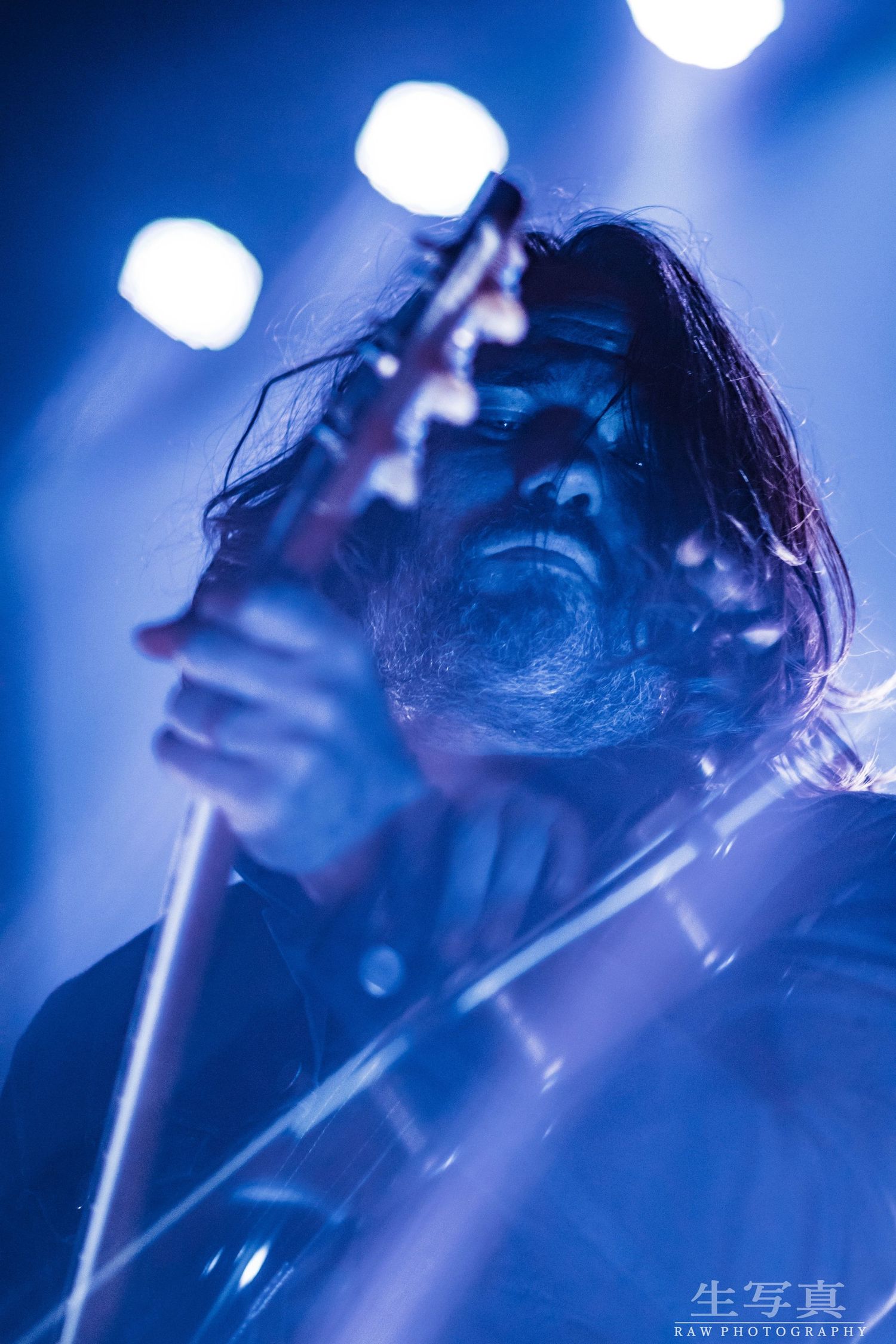 Dramatic blue-lit concert performance with microphone silhouetted against bright stage lighting.