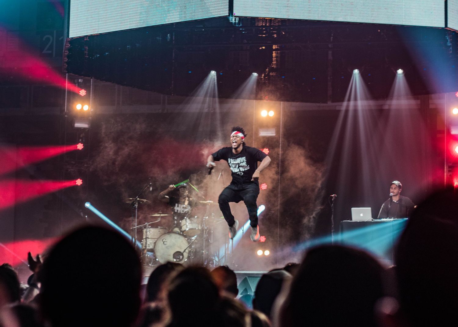 Concert performer jumping mid-air on smoky stage with dramatic red lighting effects.