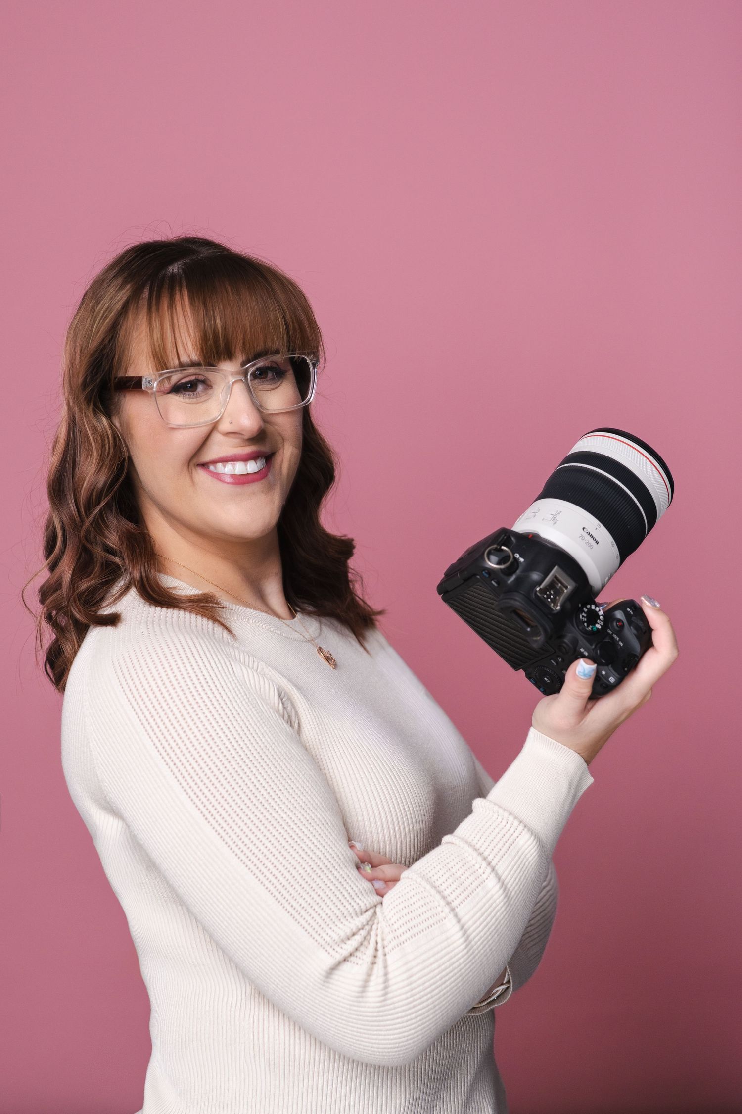Person in cream sweater holding camera against pink background.