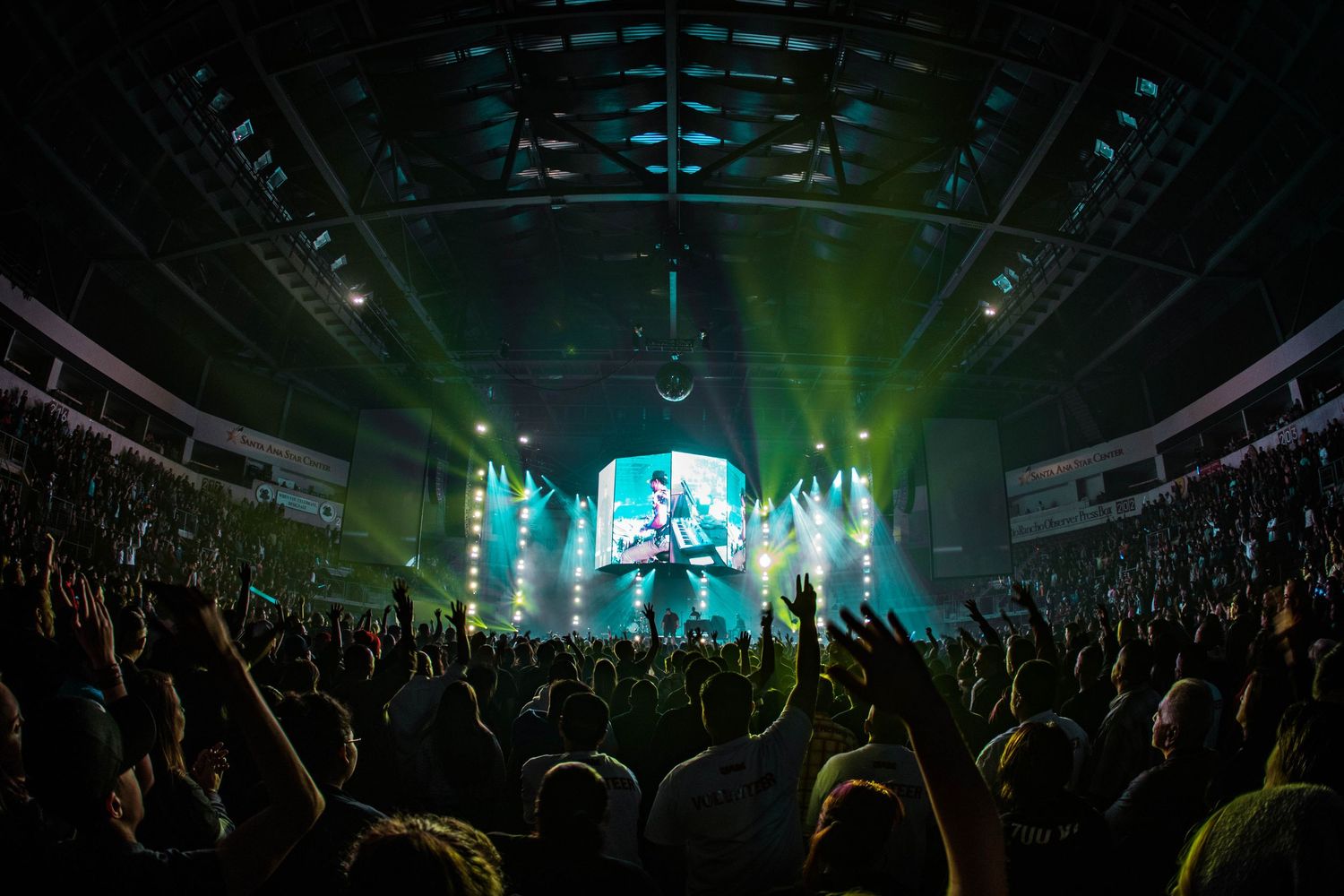 Concert crowd illuminated by green stage lights during a live performance.