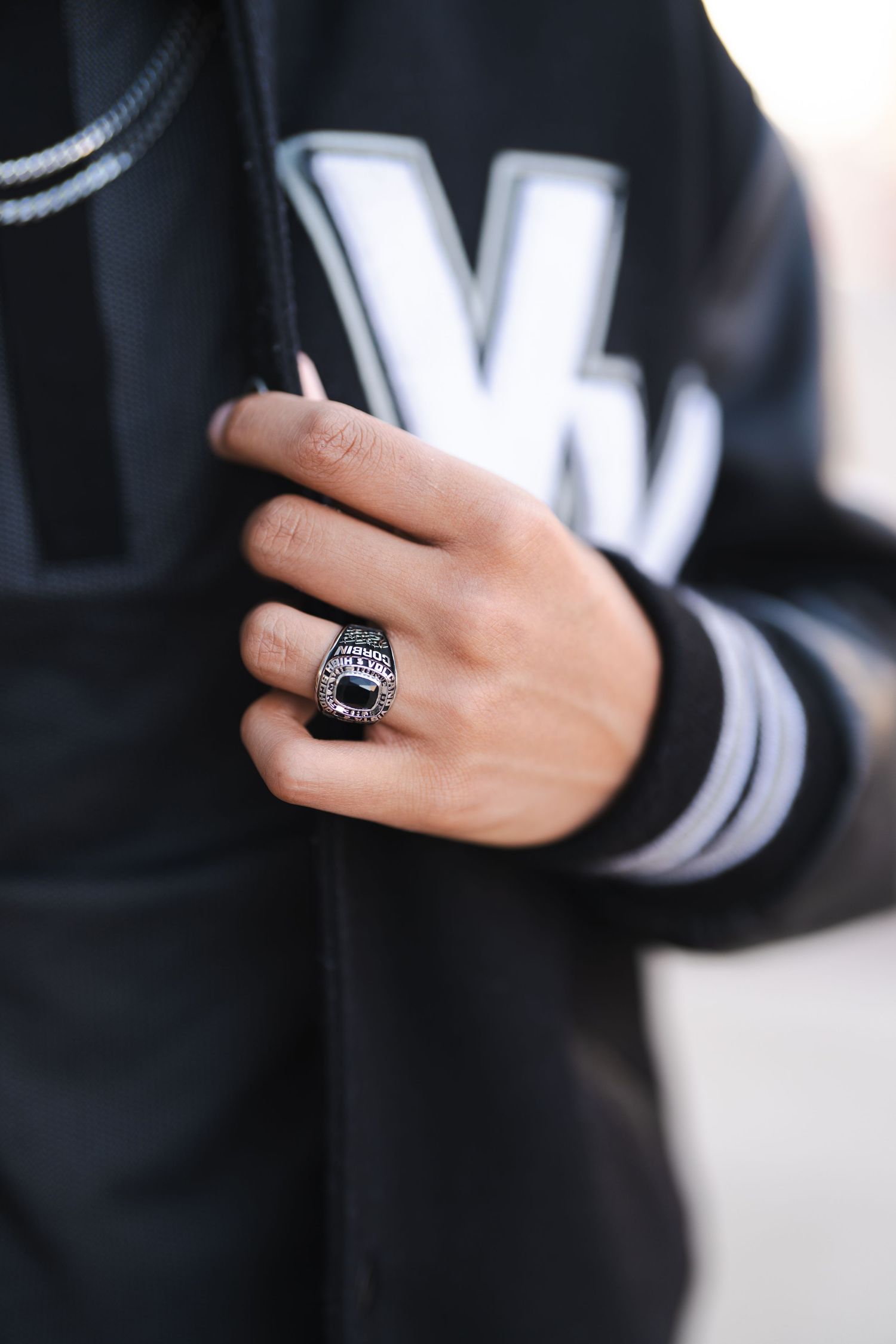 Close-up of a hand wearing a black varsity jacket and silver ring against a dark background.