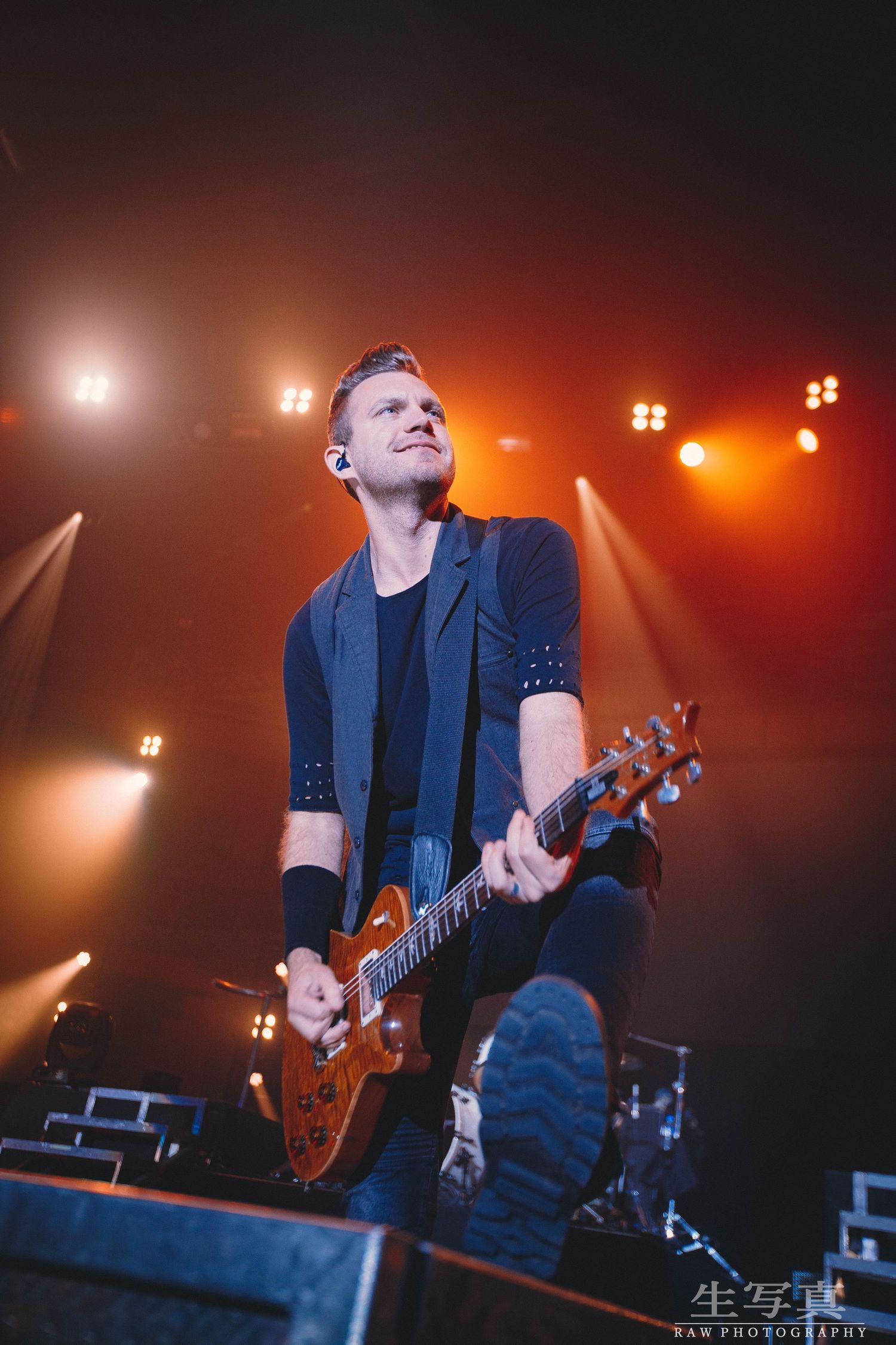 Guitarist performing on stage with warm orange lighting and dramatic shadows.