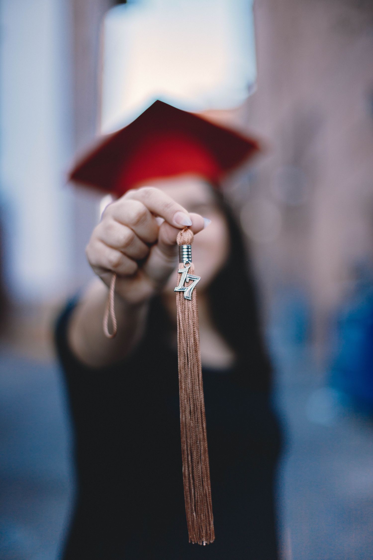 Close-up of hand holding graduation tassel against blurred background.