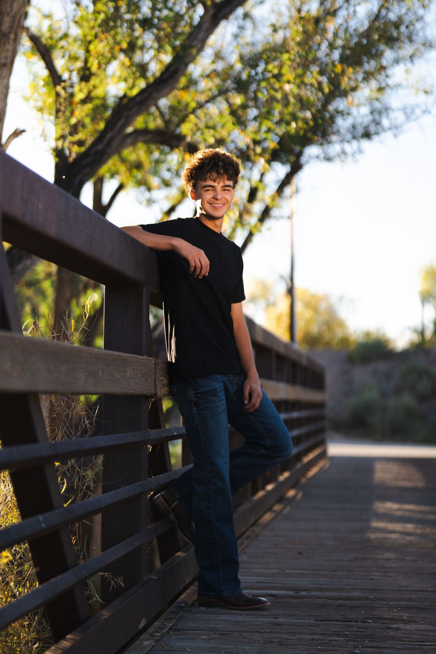 Person in black t-shirt leaning against wooden bridge railing at sunset.
