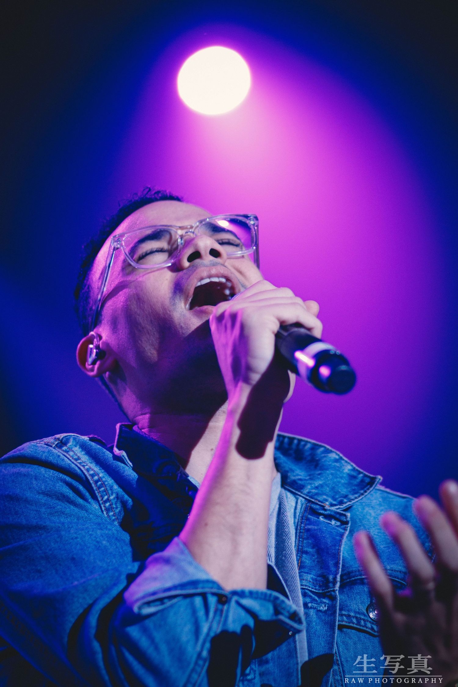 Singer performing emotionally under blue and purple stage lights with microphone.