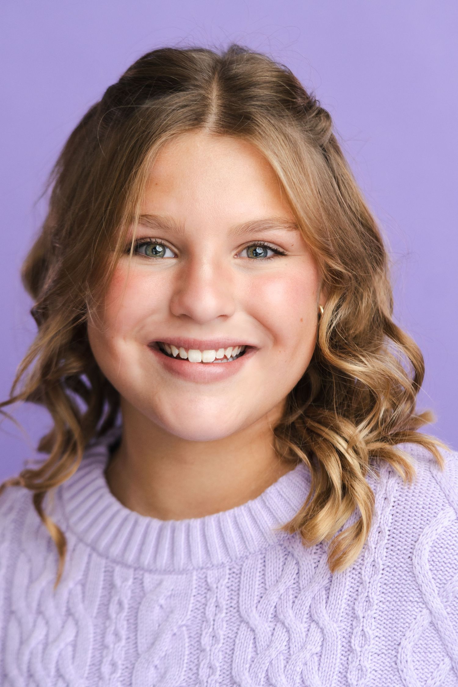 Cheerful portrait series in lavender sweater against purple background showing natural expressions.