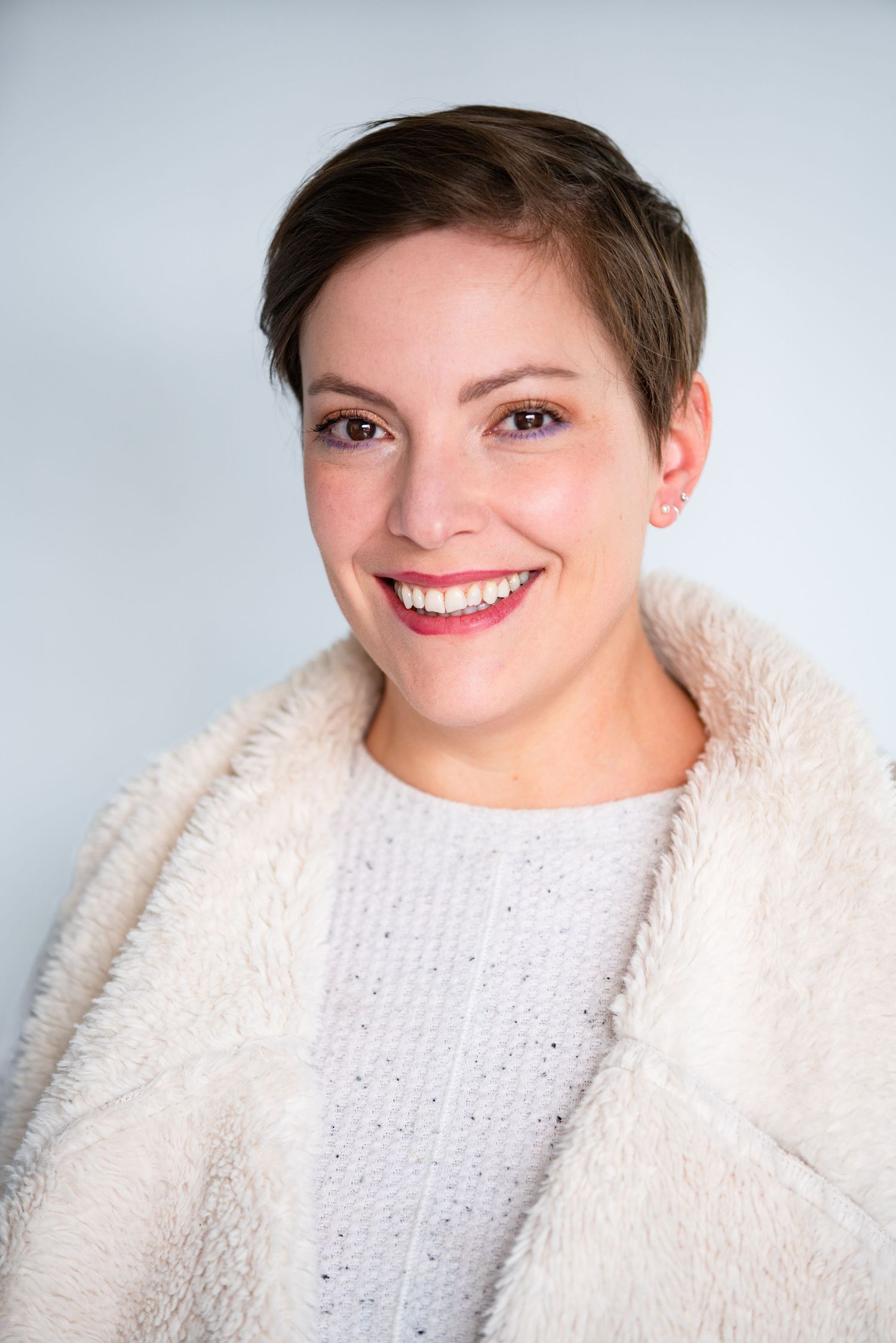 Portrait of person in white fuzzy sweater with short hair against light background.