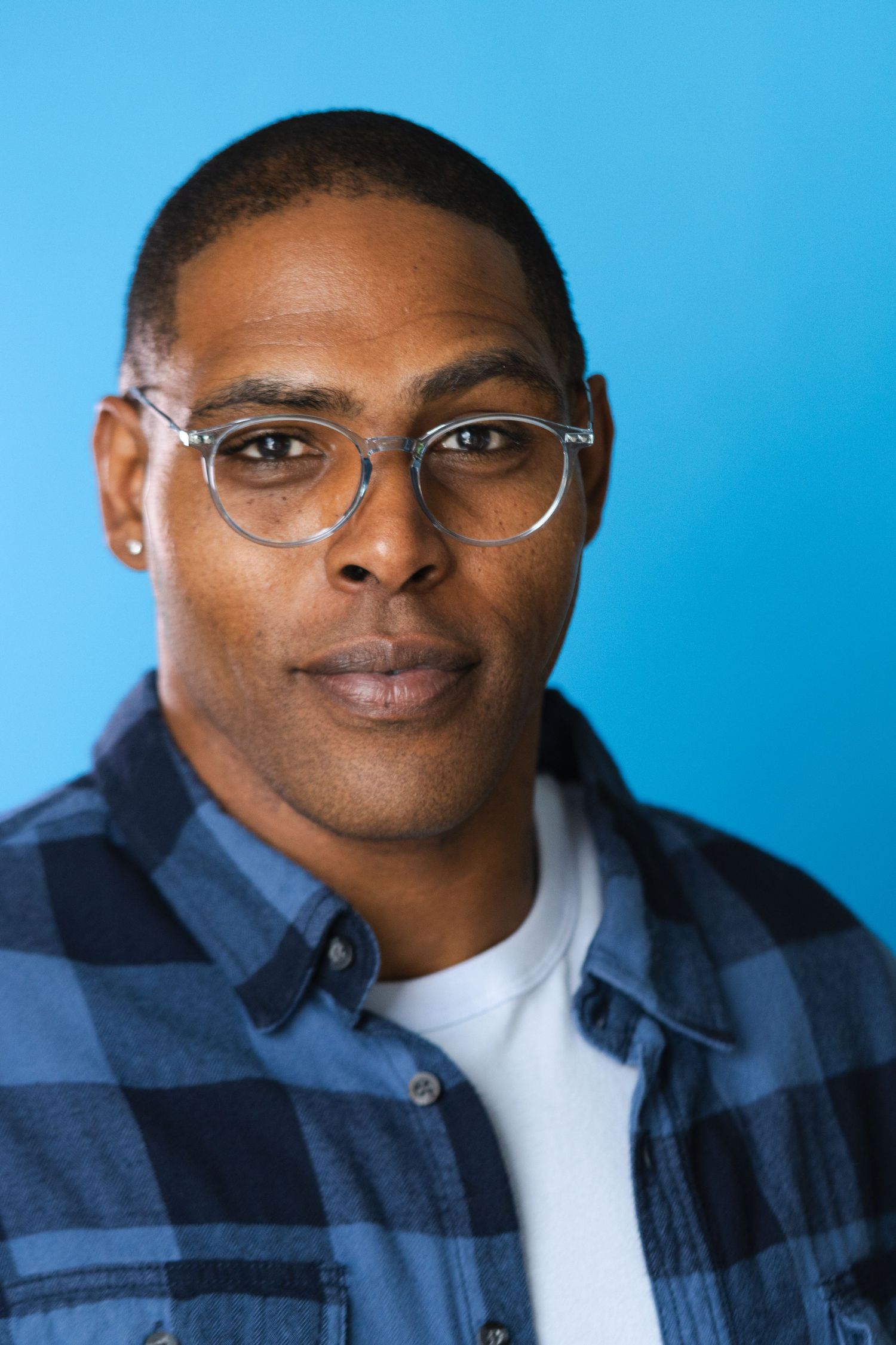 Professional headshot against blue background wearing glasses and navy jacket.