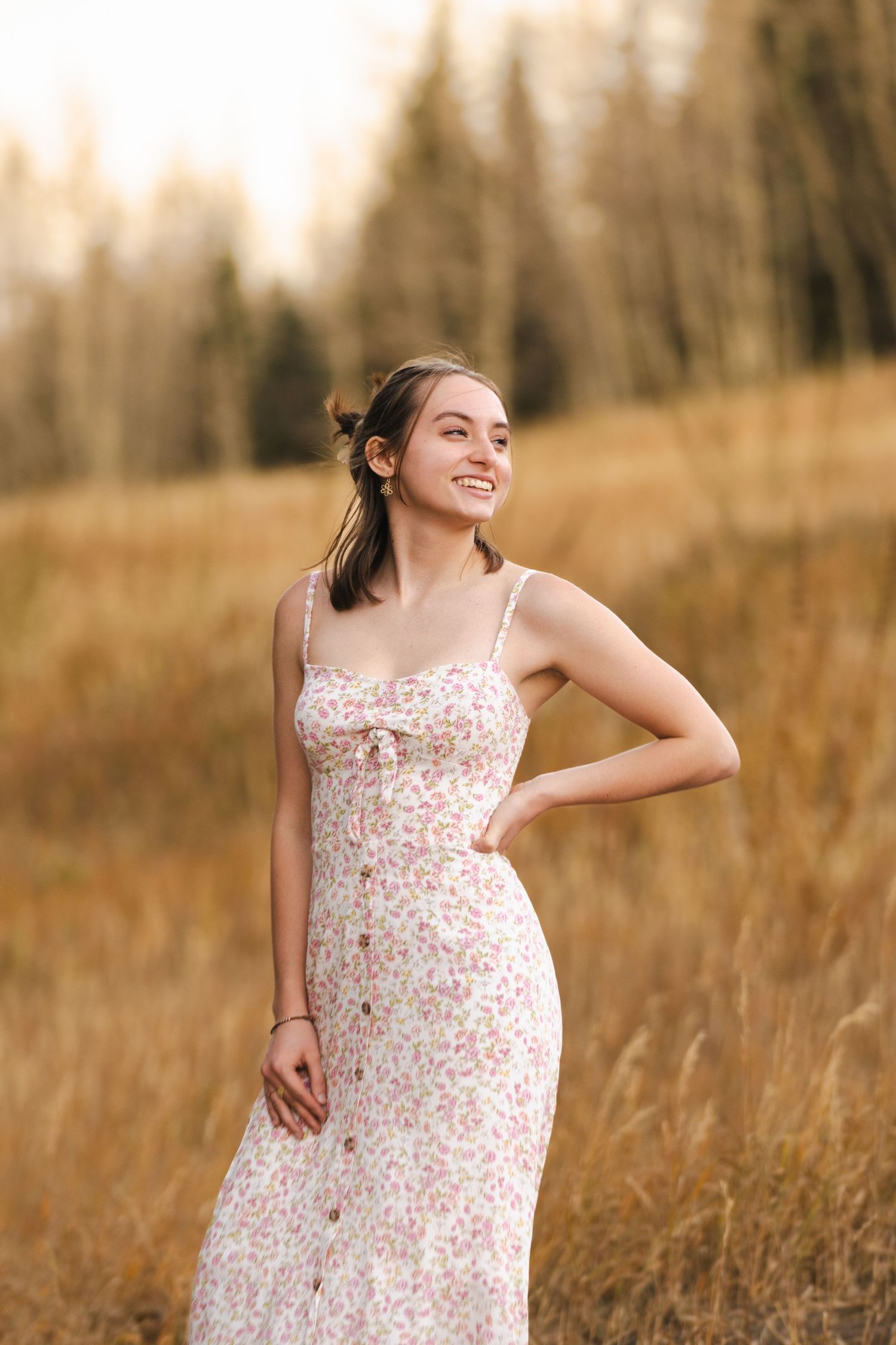 A woman in a floral dress poses in a golden field during sunset.