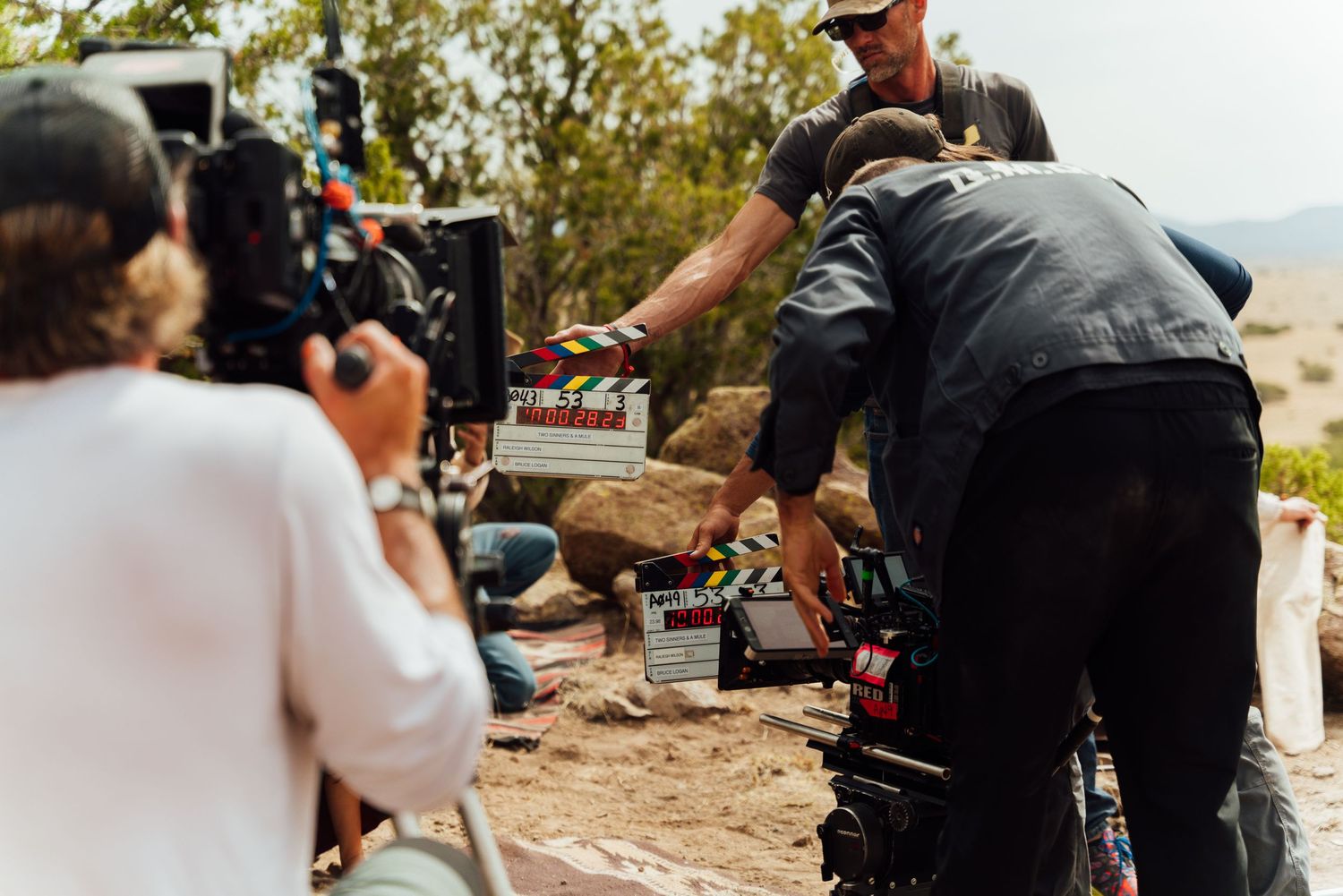 Behind-the-scenes film crew working with camera equipment on a rocky desert hillside.