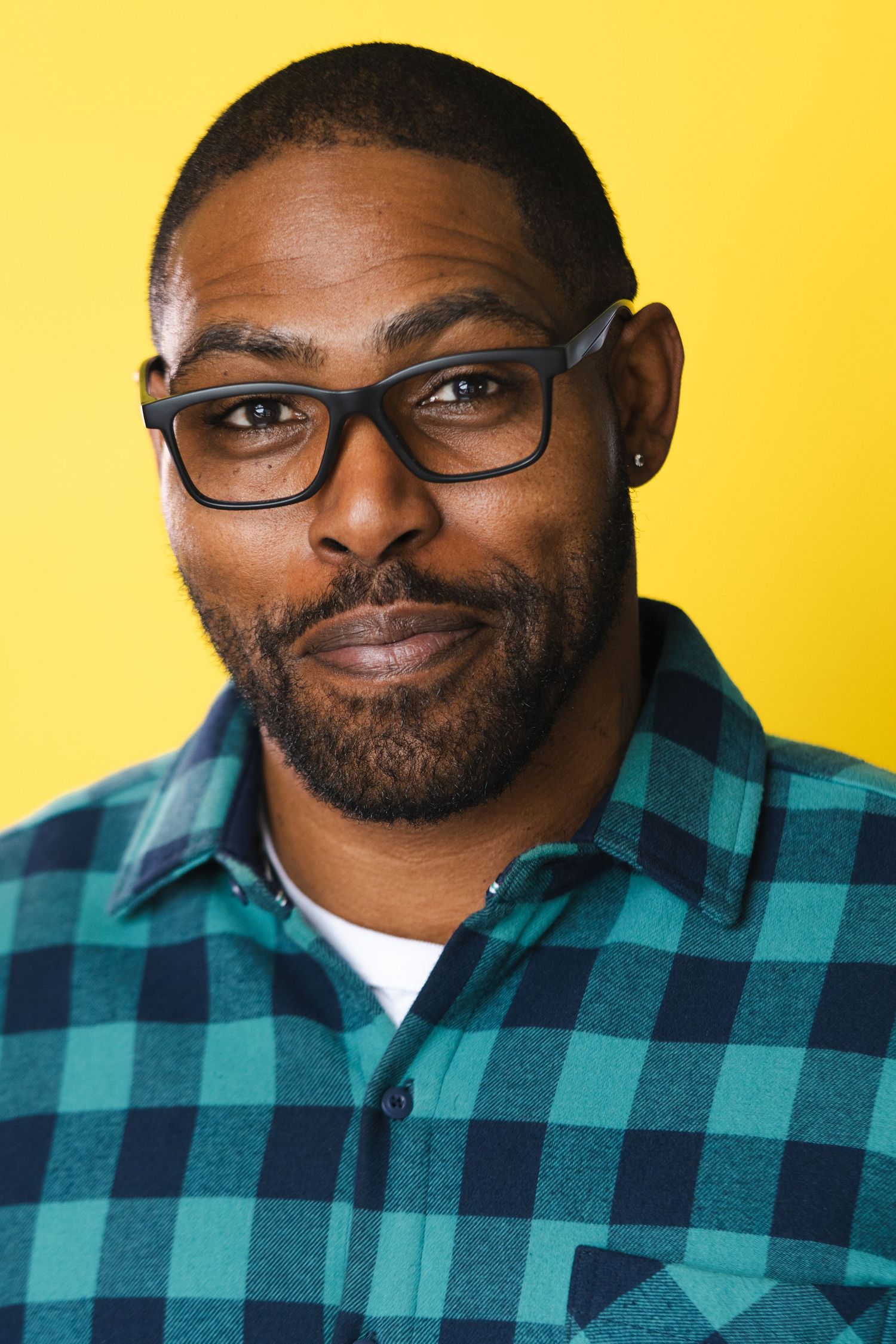 Portrait of person in plaid shirt and glasses against yellow background.