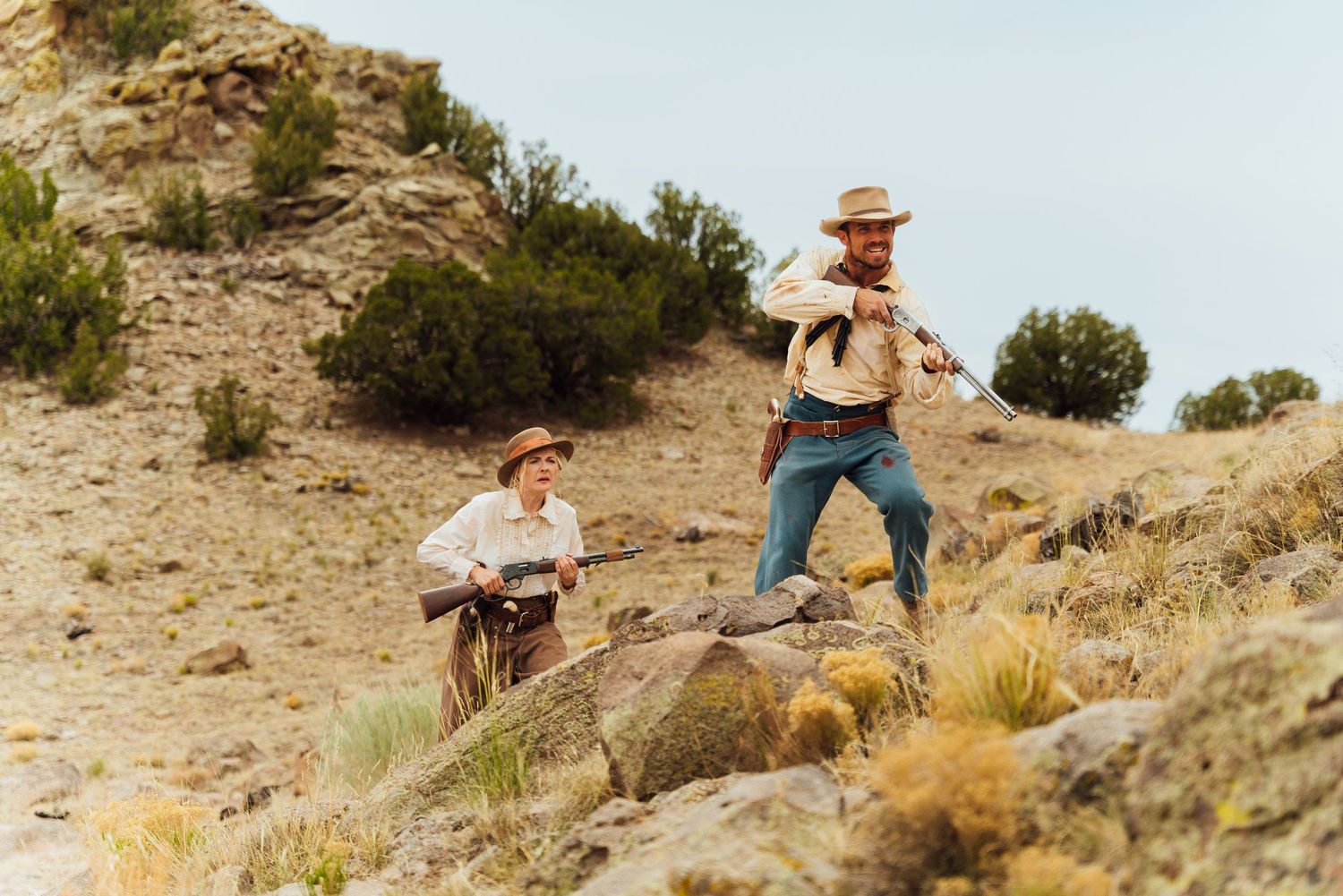 Film production crew setting up camera equipment on rugged desert terrain.