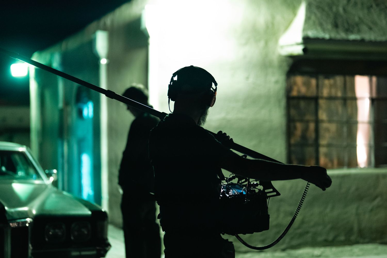 Silhouette of camera operator with equipment at night under street lights.