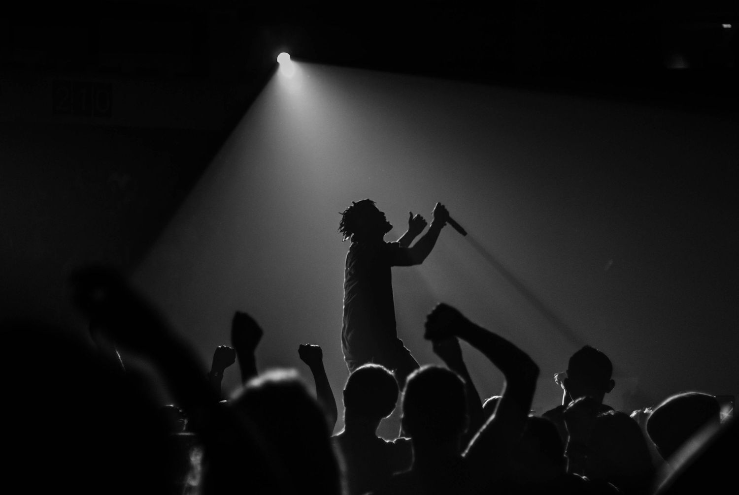 Black and white concert silhouette showing crowd surfing moment during live performance.