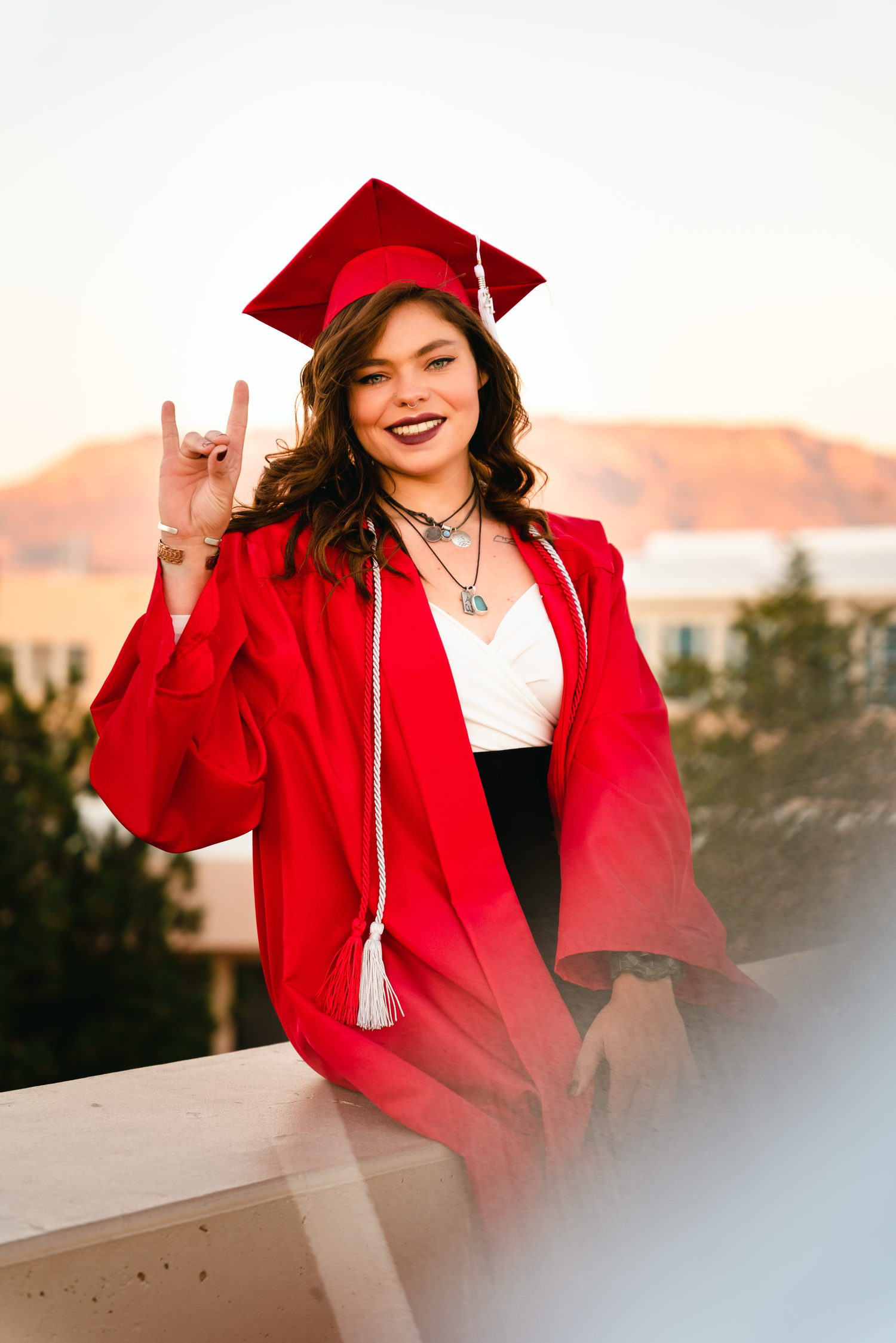 New Mexico Photographer - Graduate in bright red cap and gown making peace sign gesture outdoors.