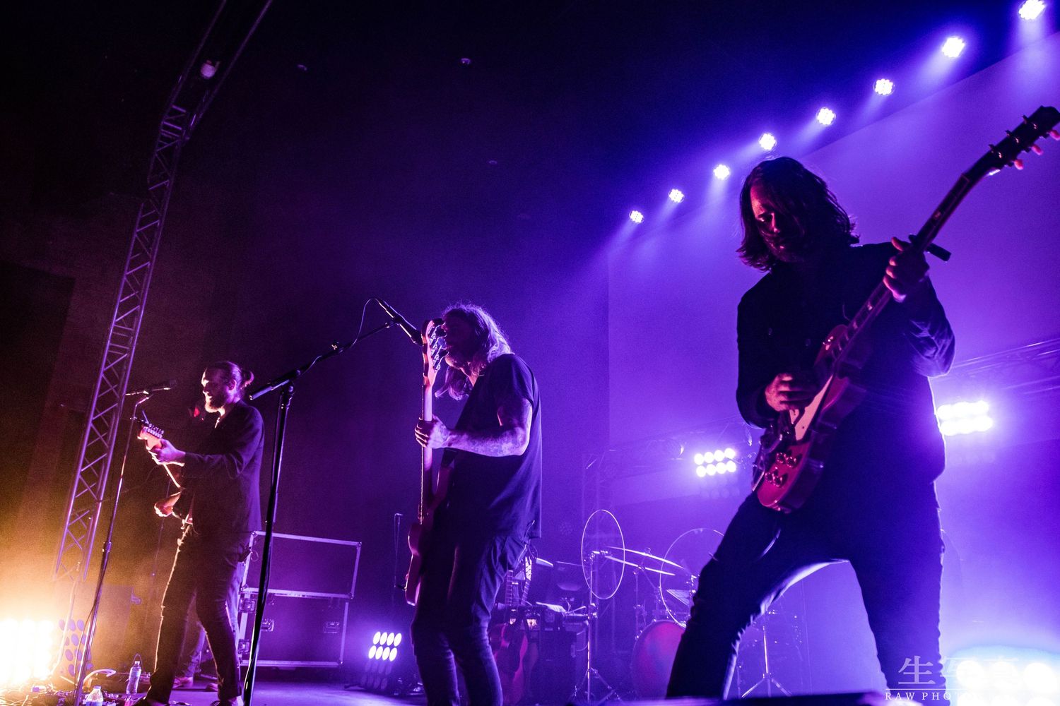 Rock band performing on stage with dramatic purple lighting and silhouetted figures.