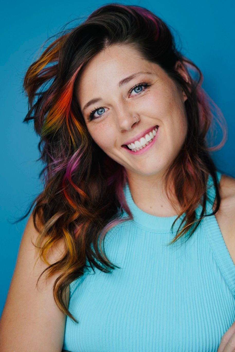 Woman in turquoise top poses playfully against bright blue backdrop.