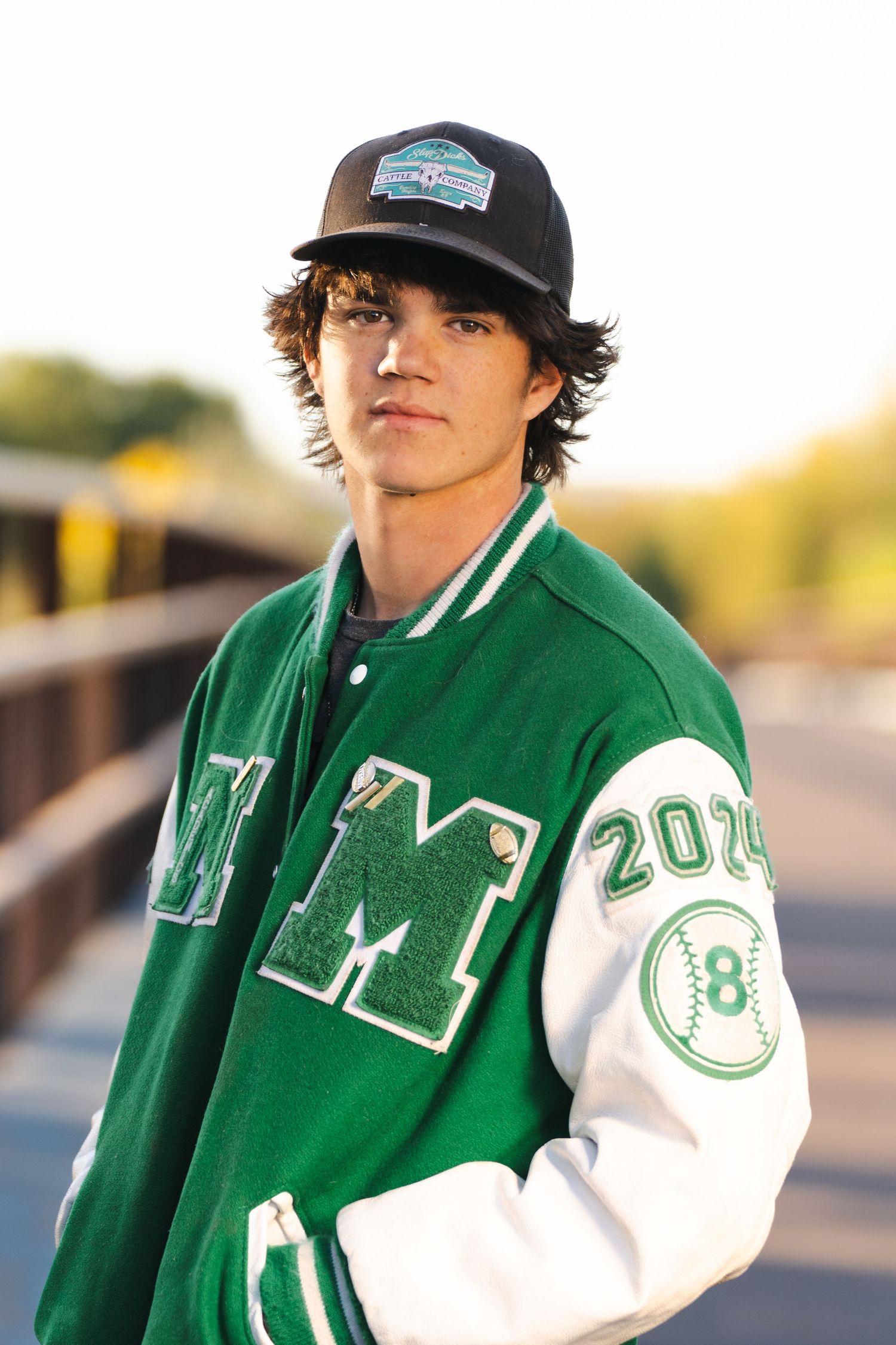 Athletic style portrait wearing green varsity jacket outdoors at sunset.