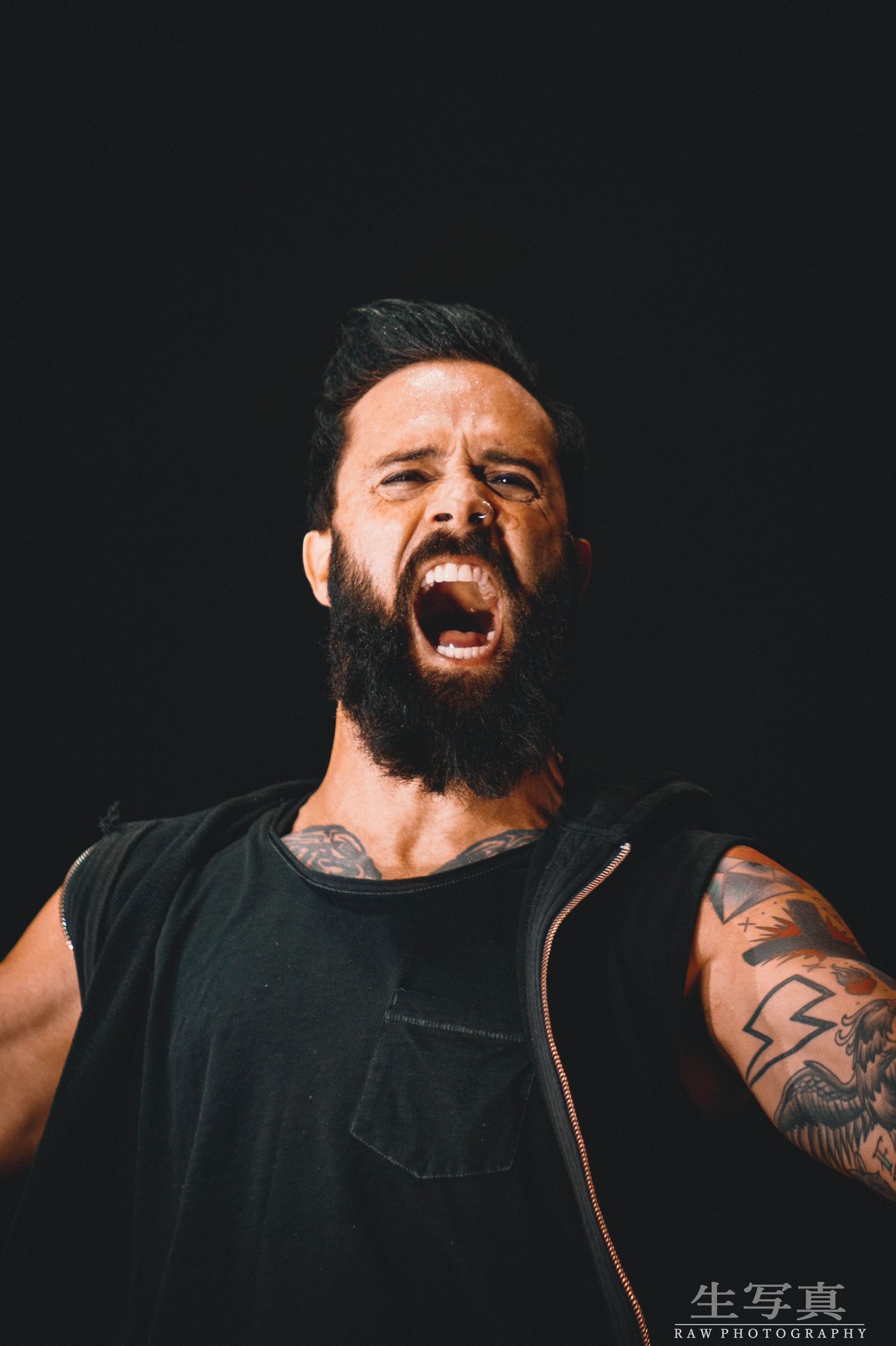 Bearded performer in black tank top showing intense emotional expression against dark background.
