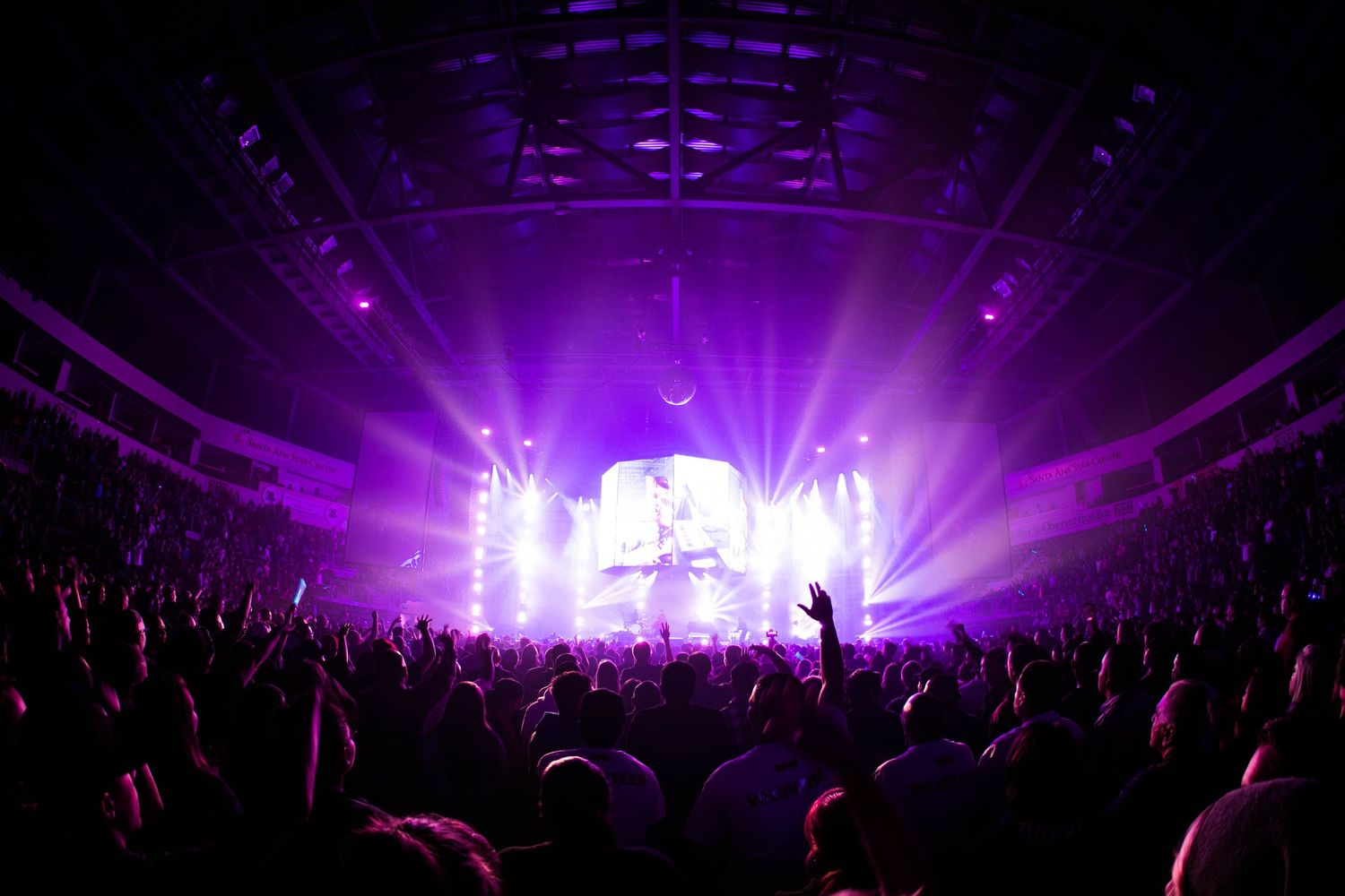 Concert venue filled with crowd silhouettes against purple stage lighting and visual effects display.