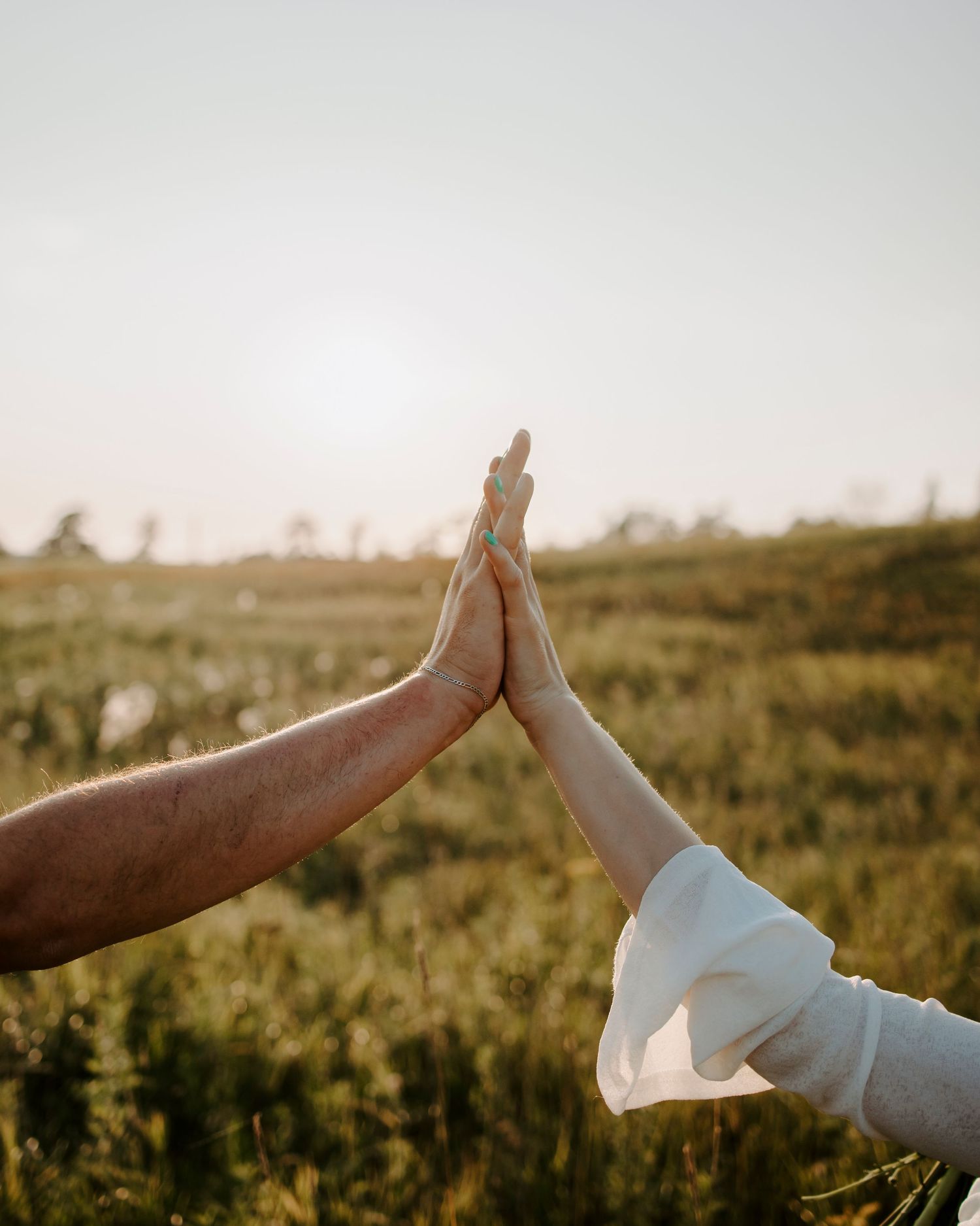 Two hands coming together in a high five gesture against a sunset lit field background.