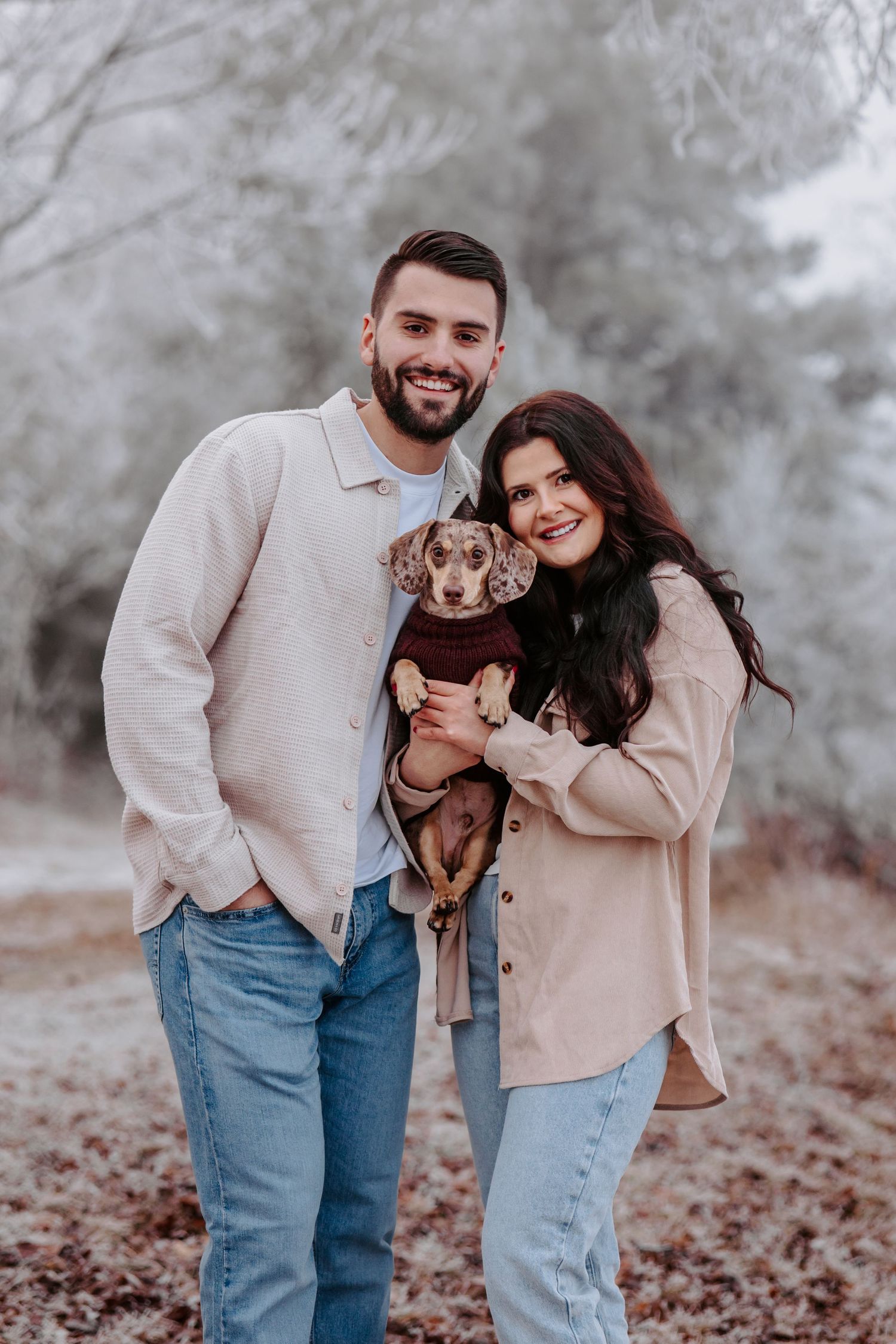 A couple poses outdoors holding their small dachshund puppy.