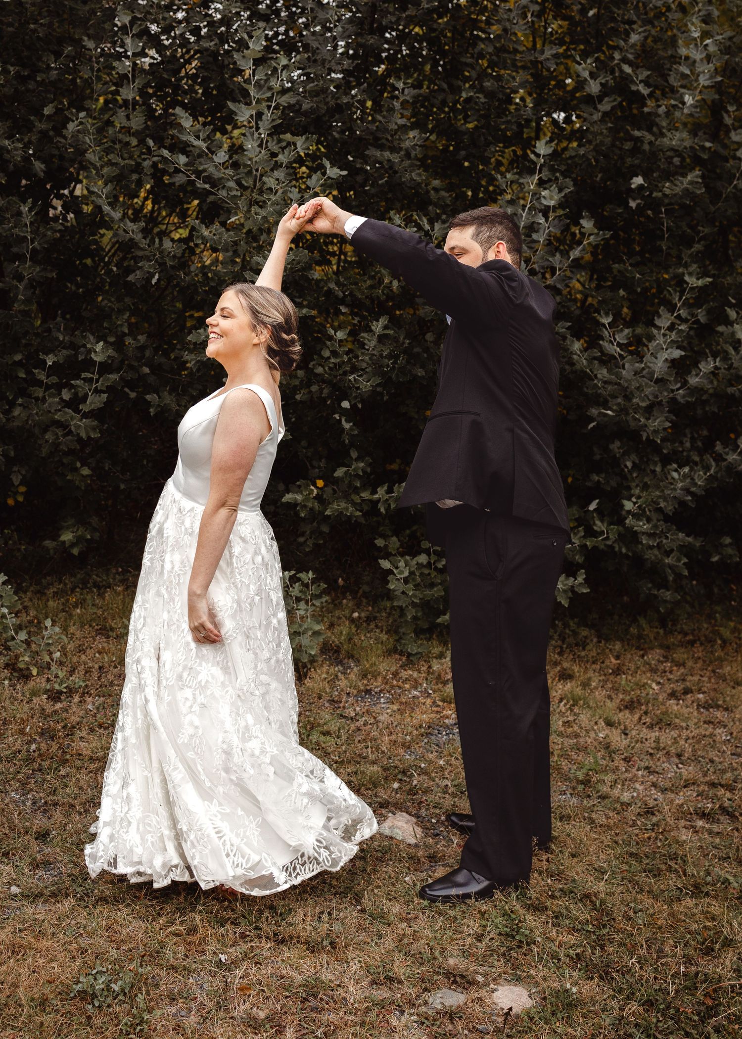 Wedding couple dancing outdoors with the groom twirling the bride in her lace dress.