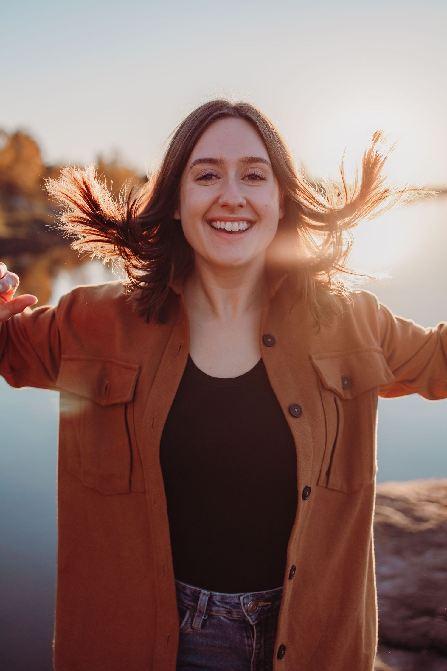 A person in a brown button-up jacket jumping joyfully with windswept hair during golden hour.