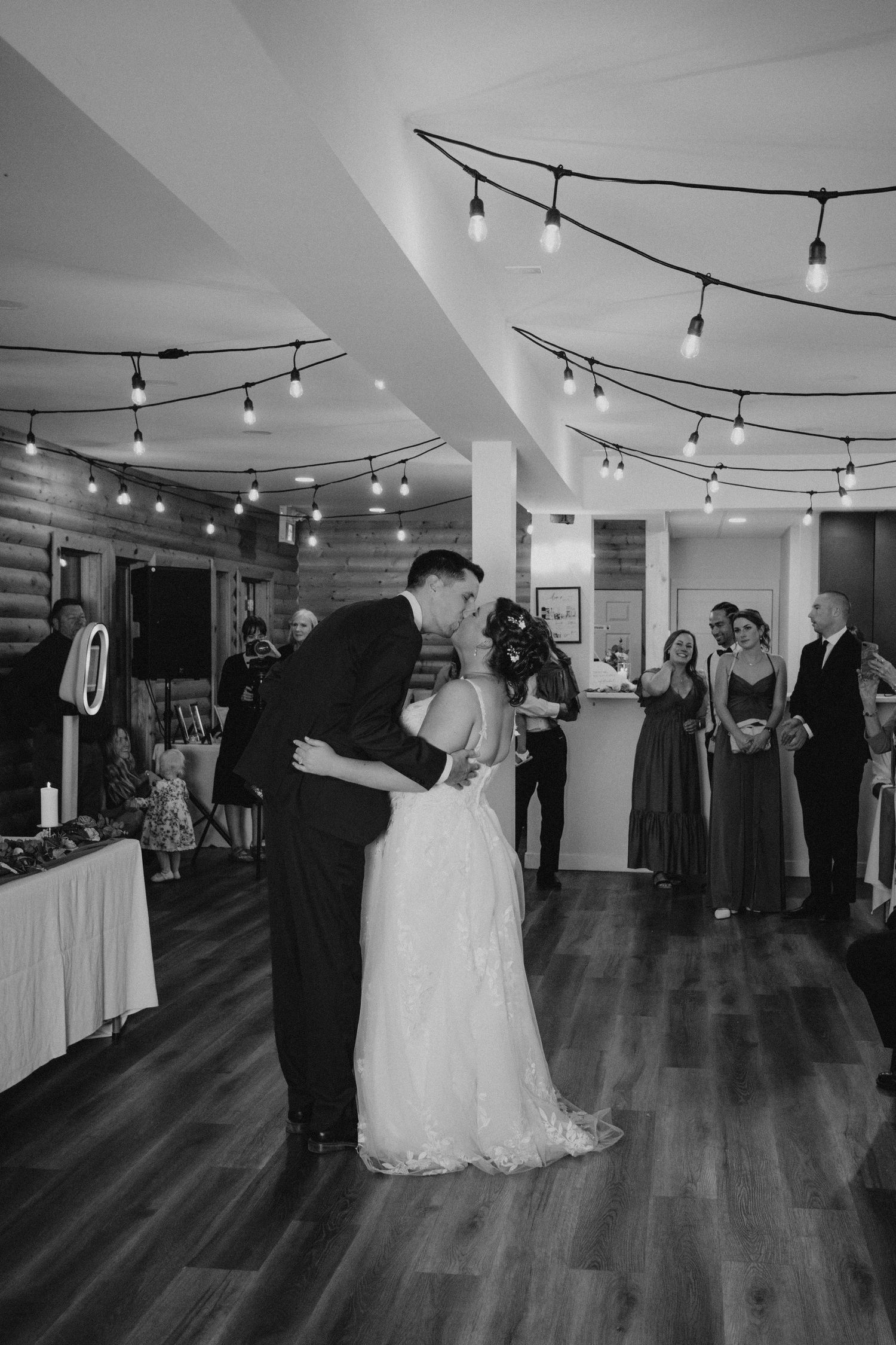 Wedding reception venue with string lights overhead and guests mingling on hardwood floors.